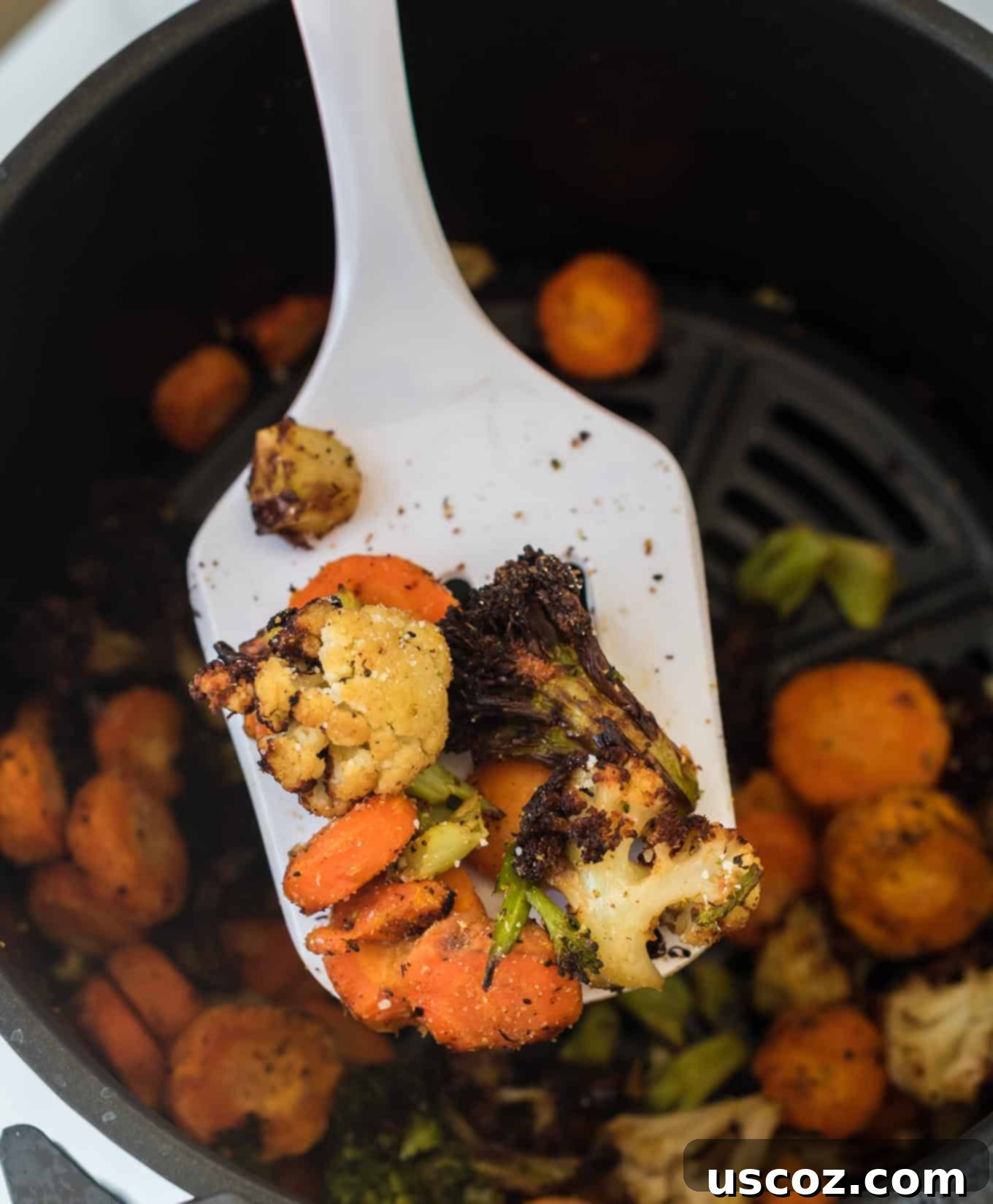 Perfect Air Fryer Frozen Vegetables 6 A white spatula scoops a generous portion of freshly air-fried, seasoned mixed vegetables from the air fryer basket.