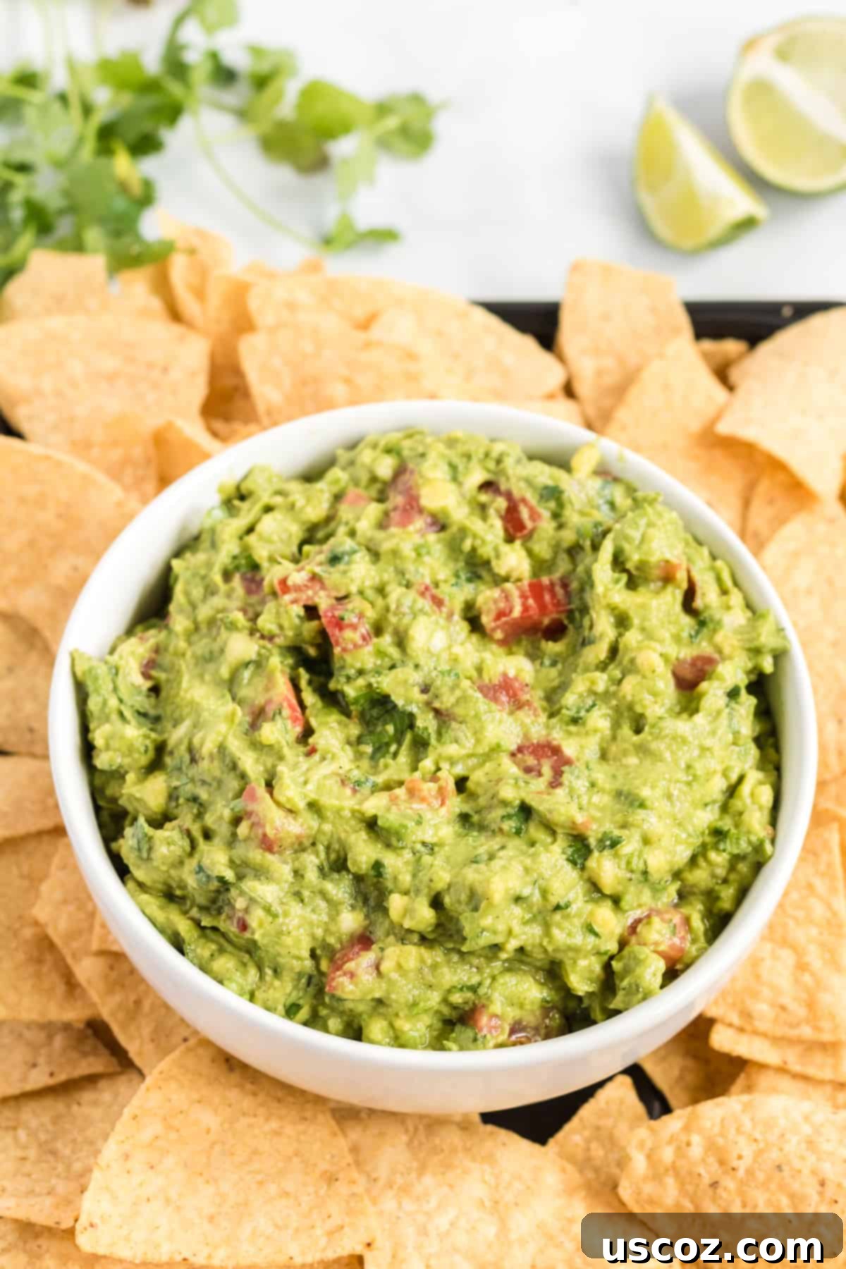 Your New Favorite Guacamole Recipe 2 Delicious homemade guacamole in a bowl, surrounded by crispy tortilla chips on a rustic platter, ready for serving.