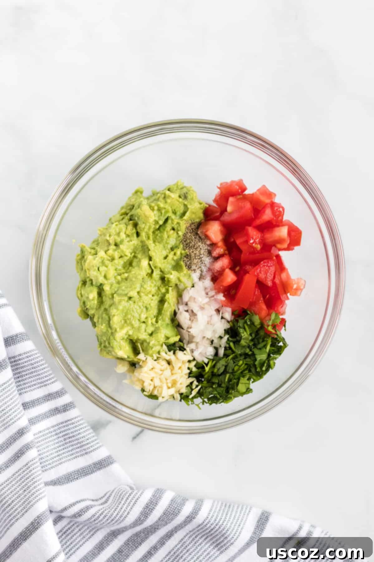 Your New Favorite Guacamole Recipe 4 A bowl filled with mashed avocado, minced shallot, garlic, chopped cilantro, and diced Roma tomatoes, showcasing the pre-mixed ingredients for guacamole.