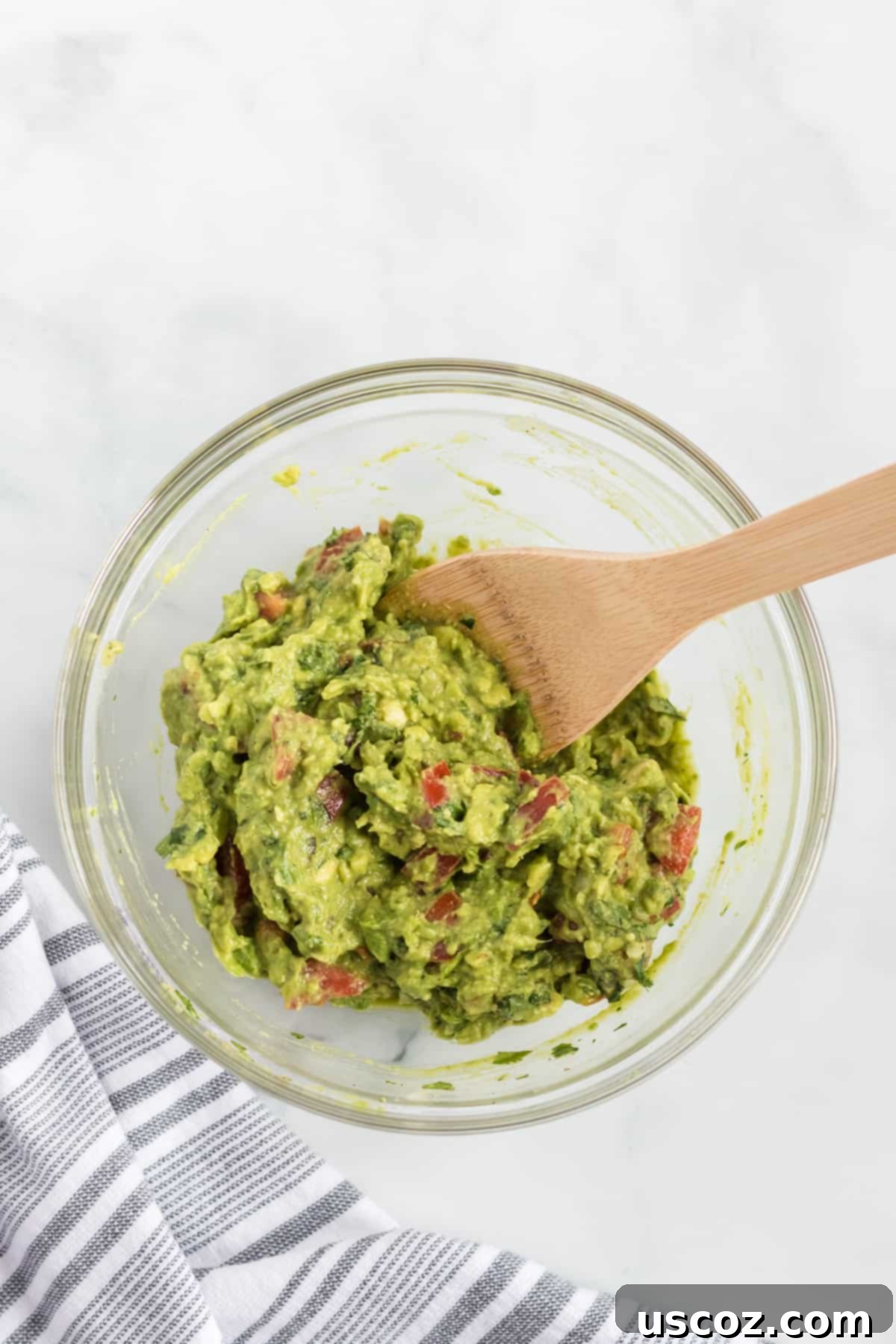 Your New Favorite Guacamole Recipe 5 Freshly made guacamole mixed with a wooden spoon in a white bowl, showing its vibrant green color and chunky texture.