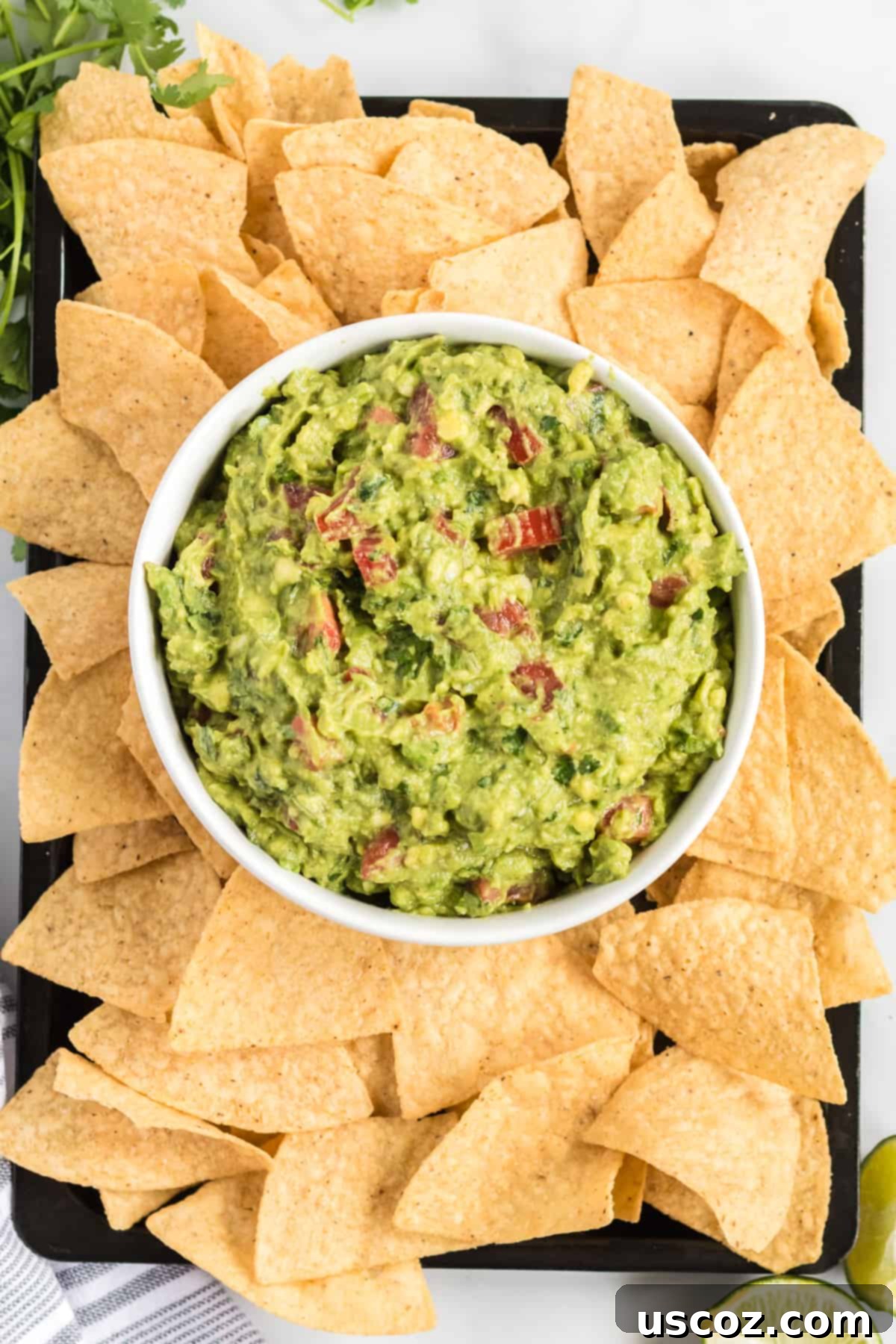Your New Favorite Guacamole Recipe 8 A bowl of delicious guacamole with tomatoes, surrounded by colorful tortilla chips on a large serving platter.