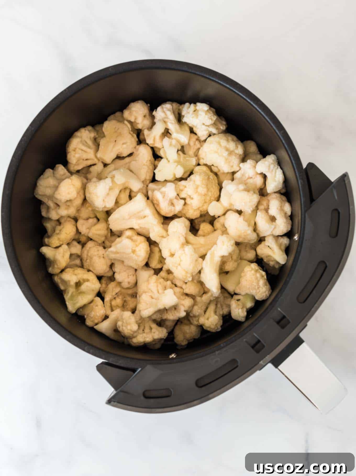 Crispy Air Fryer Frozen Cauliflower 3 Close-up view of frozen cauliflower florets evenly spread in an air fryer basket before cooking, illustrating proper loading for optimal crispiness.
