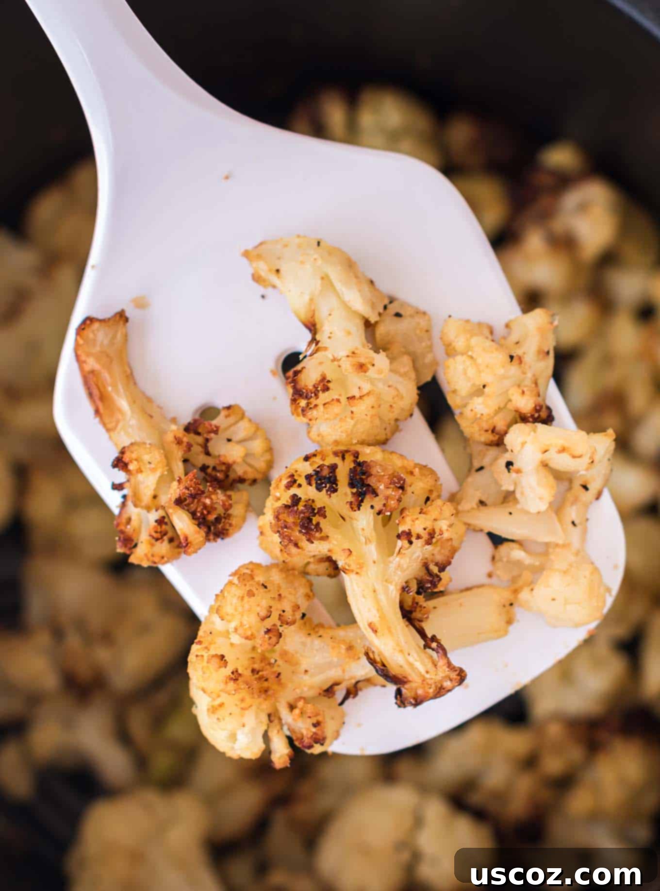 Crispy Air Fryer Frozen Cauliflower 7 A serving spatula holding a generous portion of freshly air-fried, golden-brown cauliflower florets, highlighting their crispy texture and delicious appeal.