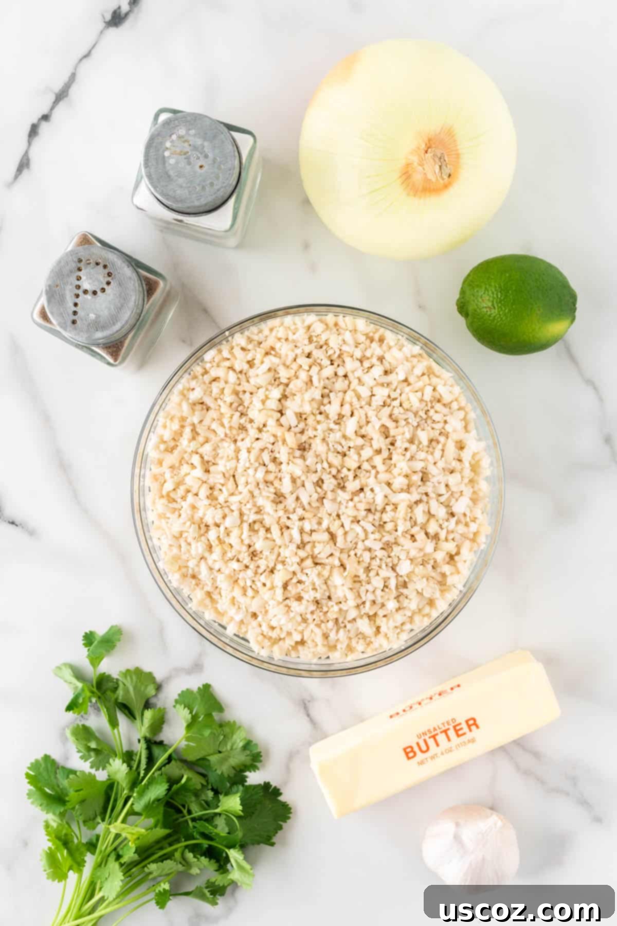 Zesty Cilantro Lime Cauliflower Rice 5 Key ingredients for cilantro lime cauliflower rice laid out: riced cauliflower, diced yellow onion, minced garlic, fresh cilantro, lime, and butter.