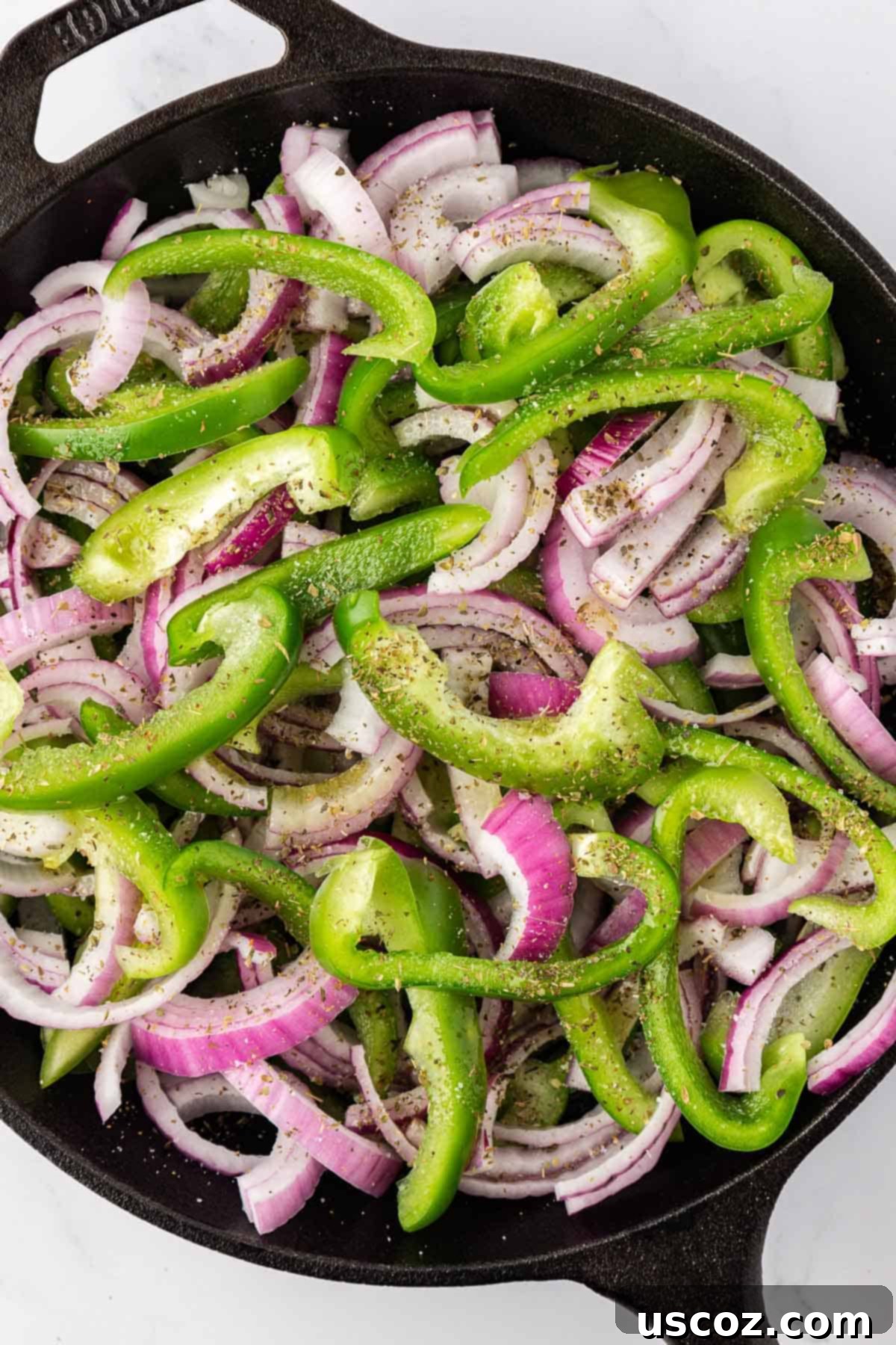Sizzling Fajita Vegetables 6 Sliced green bell peppers and red onions mixed with olive oil, salt, and oregano in a hot skillet, ready to be sautéed.