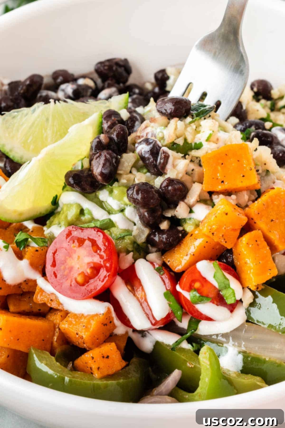 Low-Carb Cauliflower Rice Burrito Bowl 18 A vibrant cauliflower rice burrito bowl featuring black beans, fajita veggies, sweet potatoes, and guacamole, garnished and ready