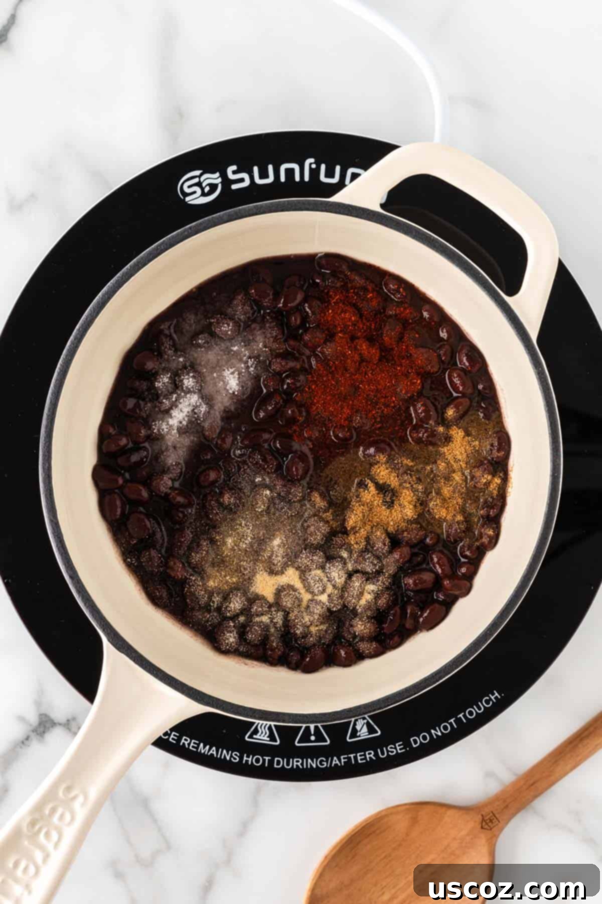 Low-Carb Cauliflower Rice Burrito Bowl 8 Adding cumin and chili powder seasonings to black beans in a saucepan
