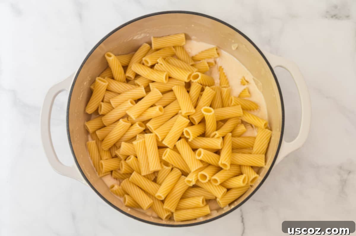 Creamy Spinach Artichoke Pasta Casserole 4 Cooked rigatoni noodles coated in a rich, creamy sauce in a white dutch oven, ready for the next step