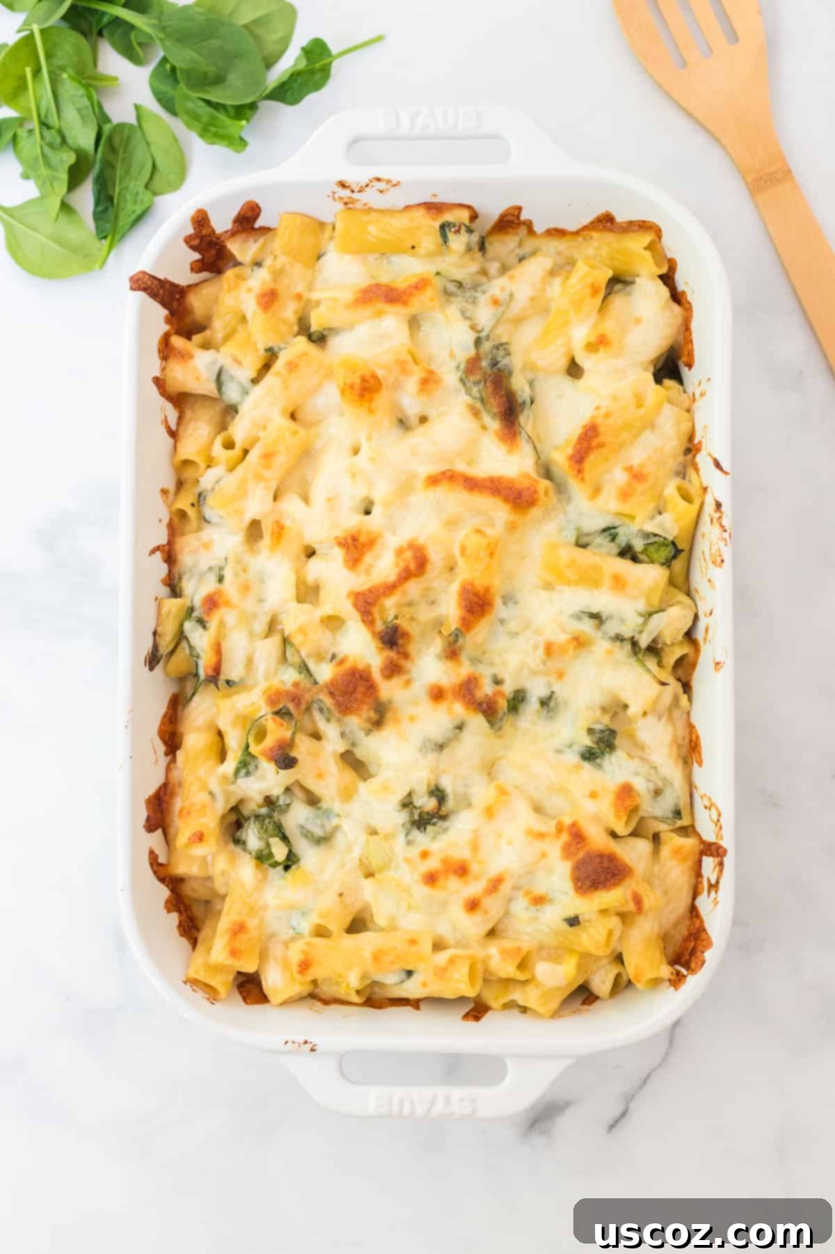 Creamy Spinach Artichoke Pasta Casserole 6 A perfectly baked spinach artichoke pasta bake in a white dish, with golden-brown, bubbly cheese on top