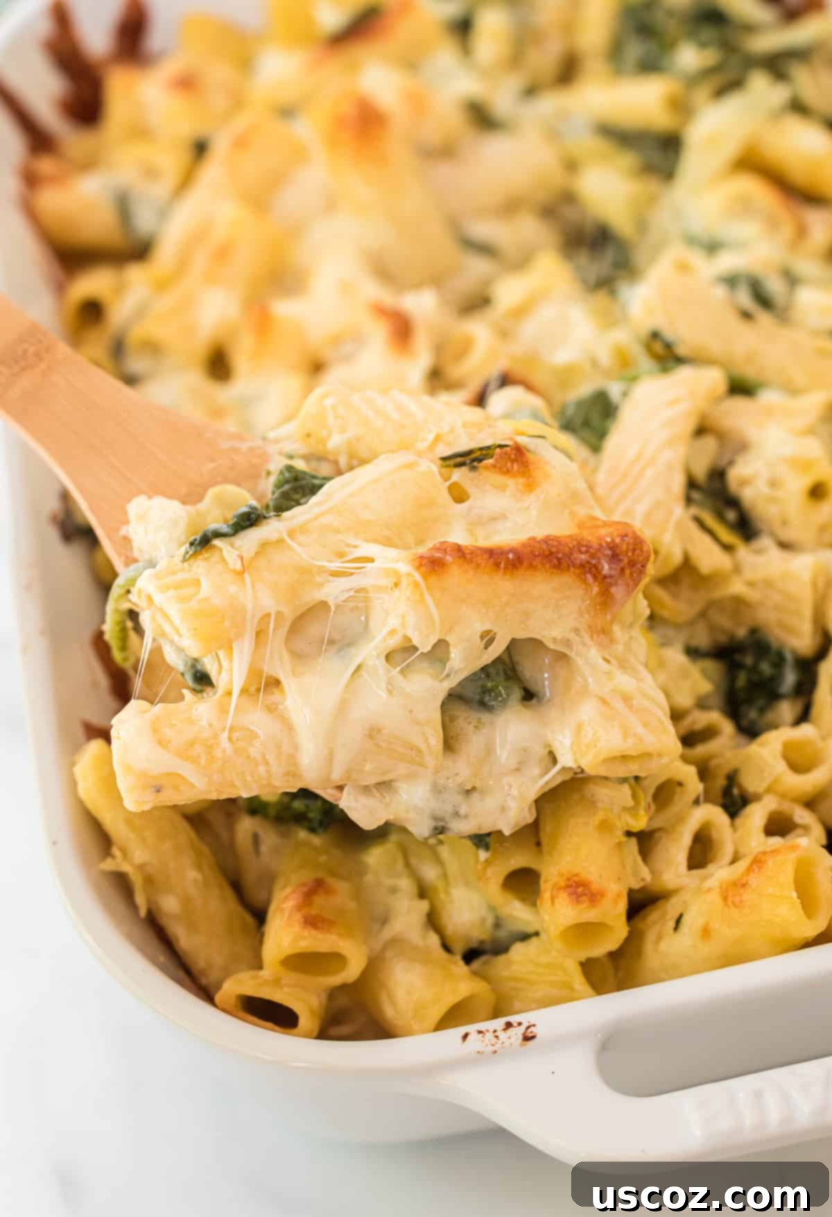 Creamy Spinach Artichoke Pasta Casserole 8 A close-up shot of a creamy spinach artichoke pasta bake, ready to be enjoyed, with a spoon taking a portion