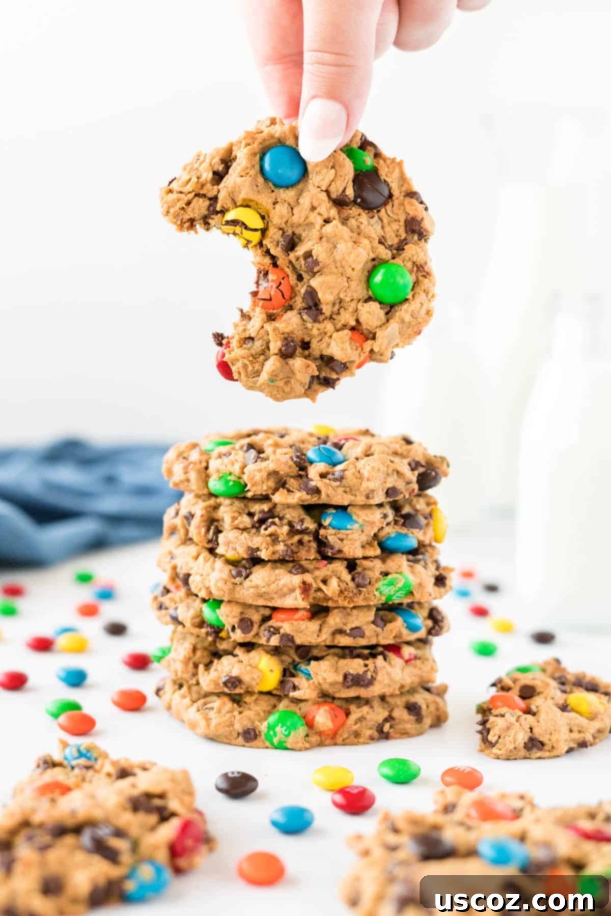 Irresistible Gluten-Free Monster Cookies 3 A hand reaches for a delicious gluten-free monster cookie, showing a bite already taken from the stack