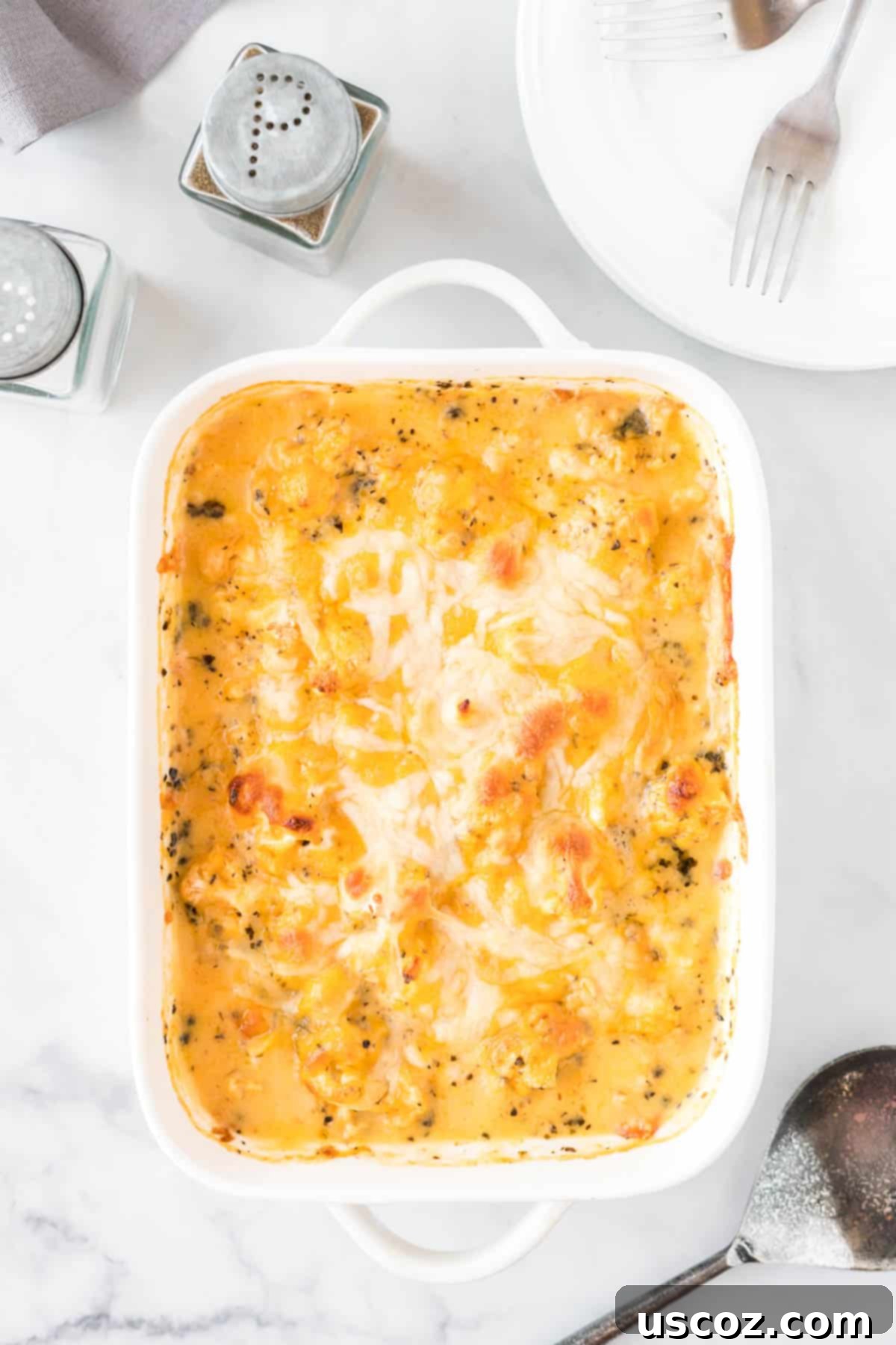 Golden Cheesy Cauliflower 8 The finished cheesy cauliflower casserole in a white ceramic baking dish, with a golden-brown, bubbly cheese topping and garnished with fresh parsley.