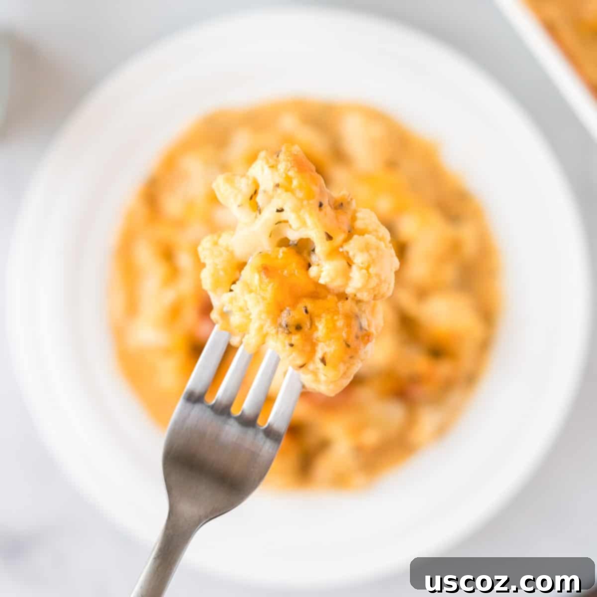 Golden Cheesy Cauliflower 9 A fork lifting a piece of cheesy cauliflower from the casserole dish, showing the melted cheese and tender cauliflower.