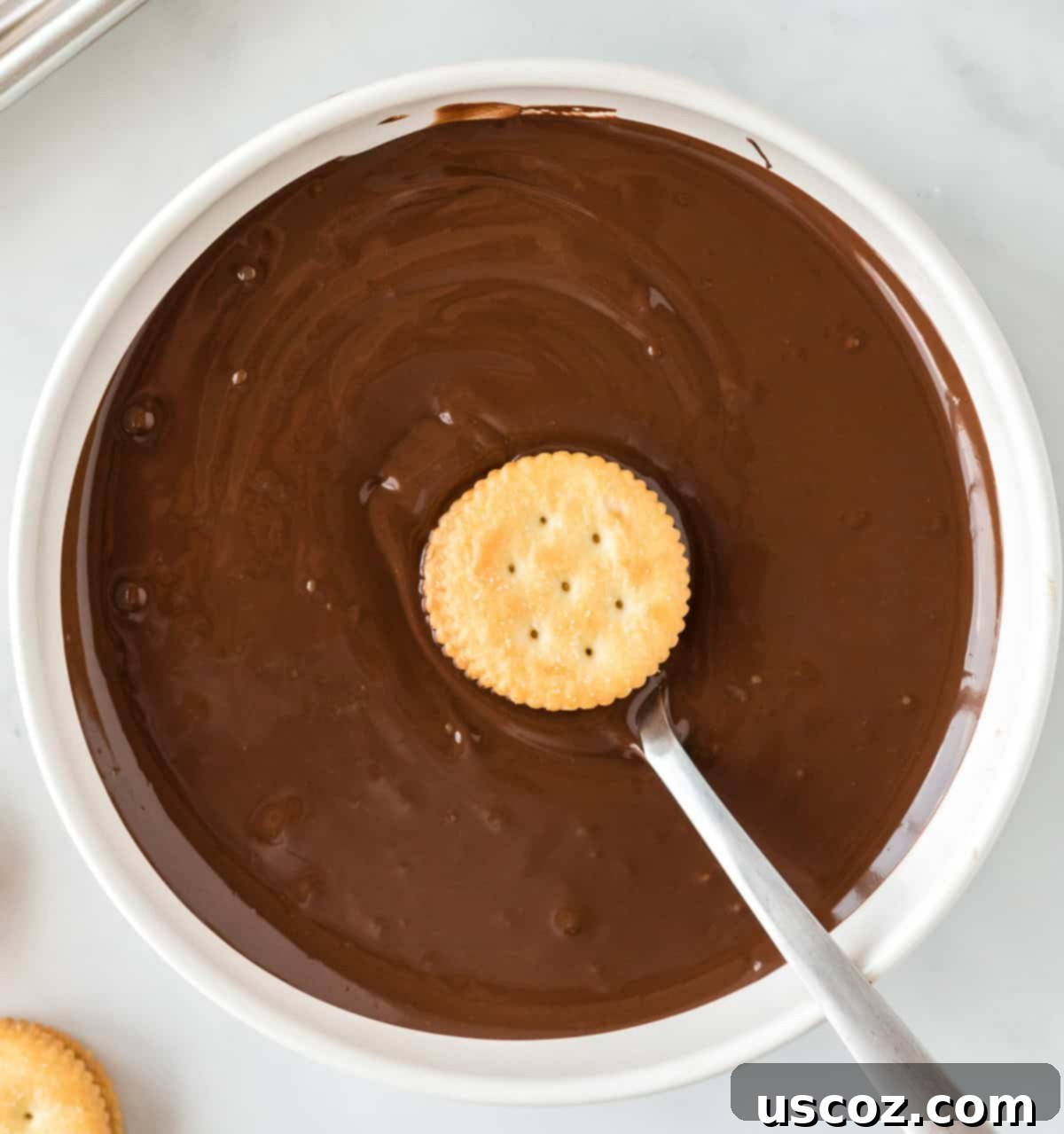 Irresistible Ritz Cookie Bites 9 A Ritz cracker sandwich being dipped into a bowl of melted chocolate with a fork.