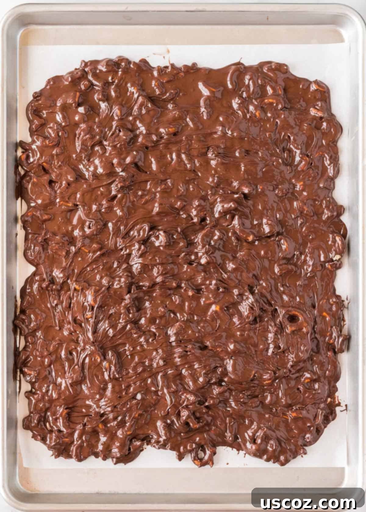 Monster Mash Bark 7 melted chocolate and pretzels spread out on a baking sheet lined with parchment paper