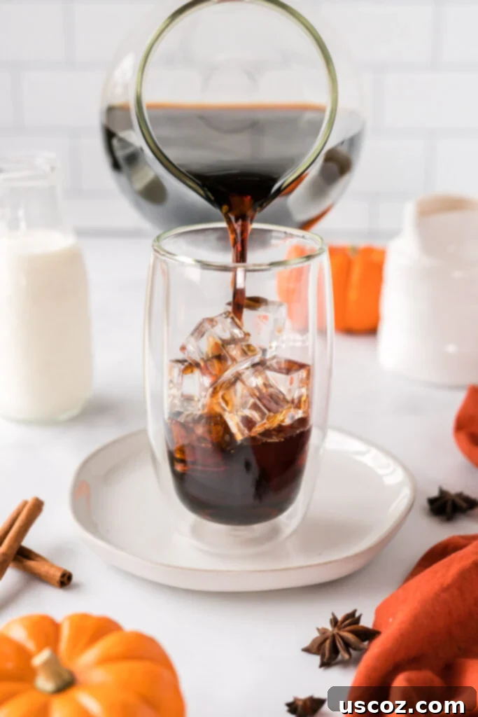 Spiced Pumpkin Cold Brew 8 Hand pouring cold brew coffee over ice in a tall glass