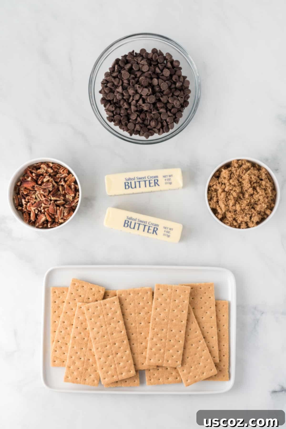 Golden Graham Toffee 4 ingredients laid out to make graham cracker toffee: graham crackers, sticks of butter, brown sugar, chocolate chips, and pecan pieces