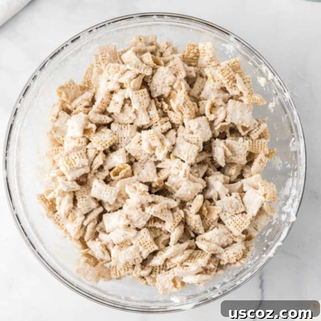 Cookies and Cream Dream Bites 11 Rice Chex cereal in a bowl being coated evenly with melted white chocolate, creating a light base for the cookies and cream flavor.
