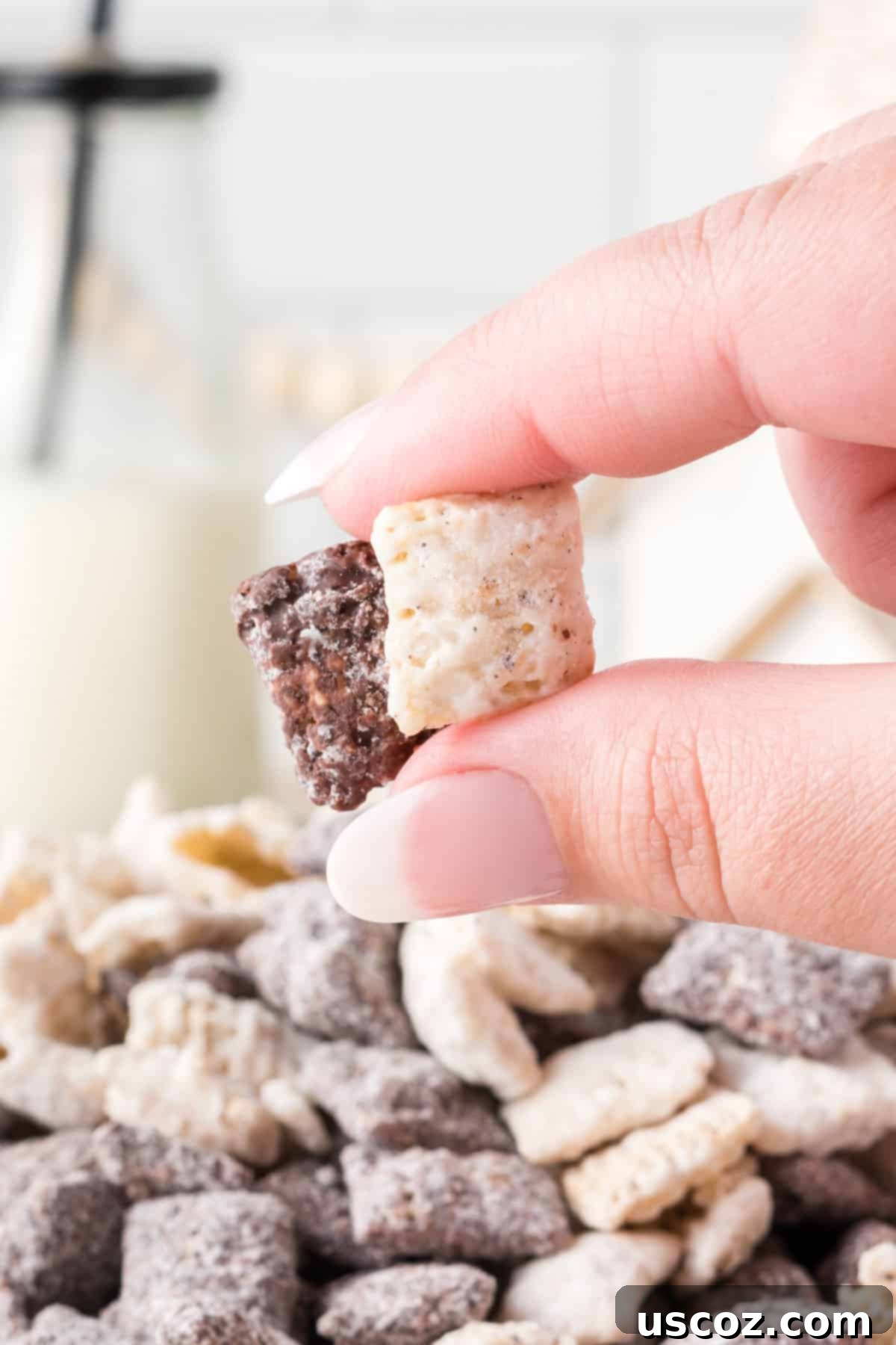 Cookies and Cream Dream Bites 15 A hand reaching into a serving bowl filled with Cookies and Cream Muddy Buddies, picking up a handful of the delicious snack.