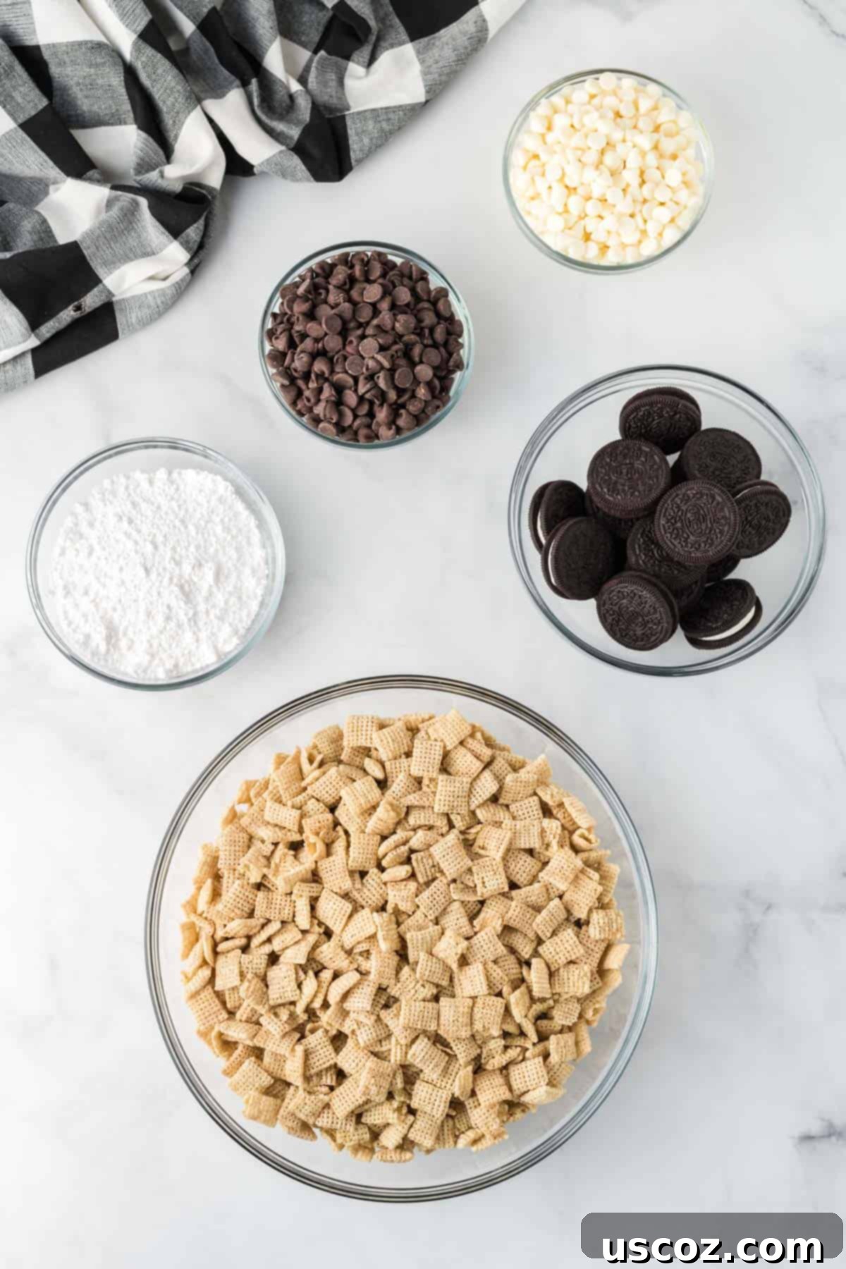 Cookies and Cream Dream Bites 4 A flat lay photograph showcasing the five key ingredients needed for Cookies and Cream Muddy Buddies: a box of Rice Chex cereal, bags of semi-sweet and white chocolate chips, a package of Oreos, and a bowl of powdered sugar.