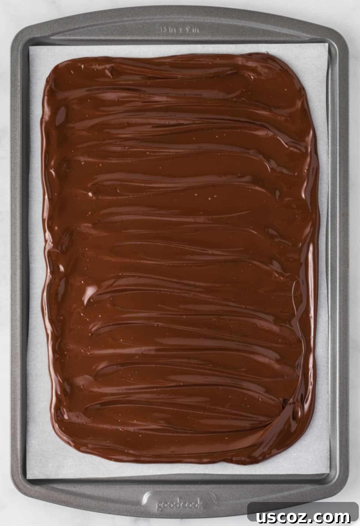 Decadent Mint Chocolate Bark 7 A thin, even layer of melted dark chocolate spread on a parchment paper-lined baking sheet, forming the base of the peppermint bark.