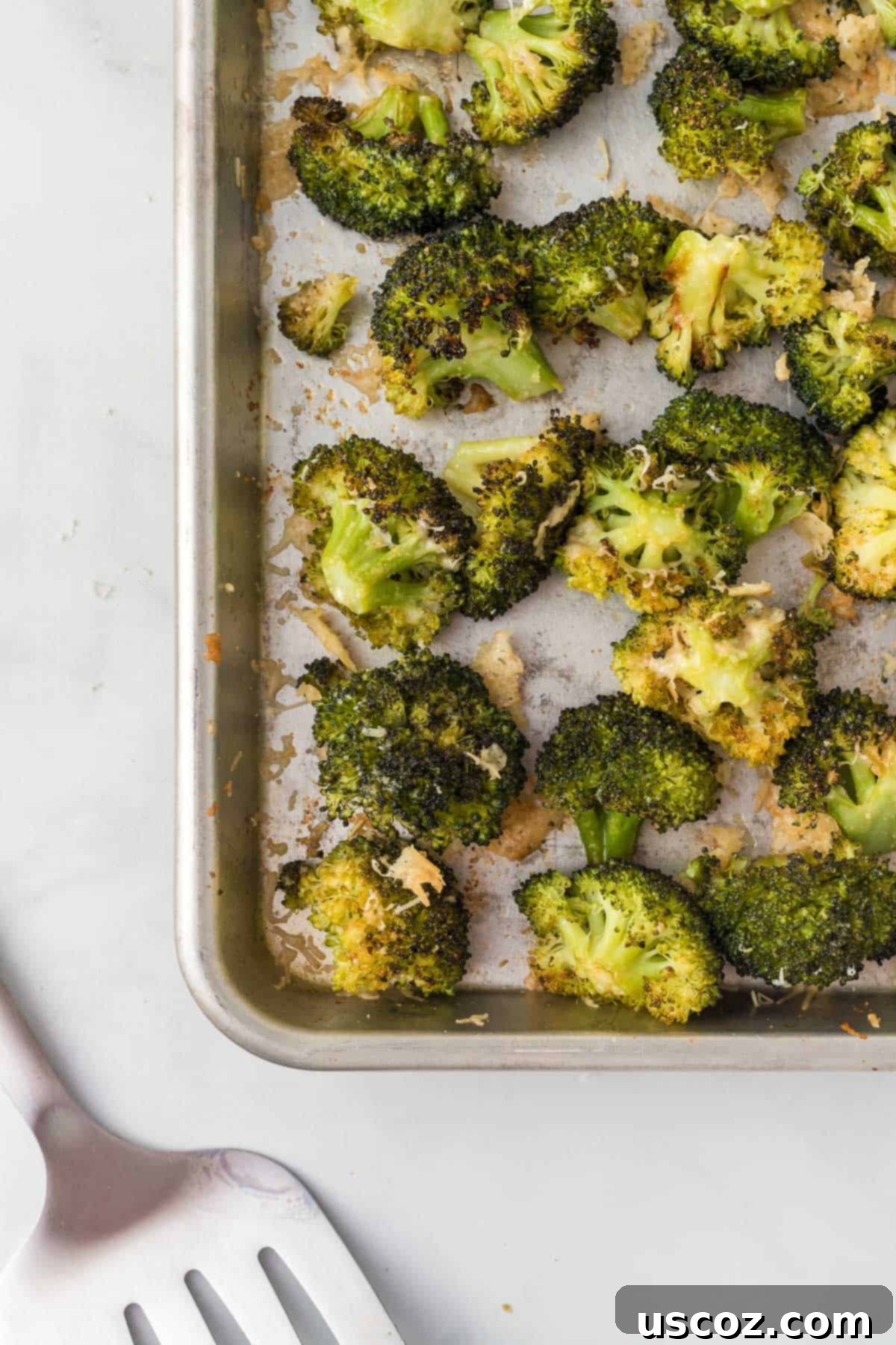 Parmesan Roasted Broccoli 2 Crispy roasted broccoli florets on a baking sheet, golden brown with melted parmesan