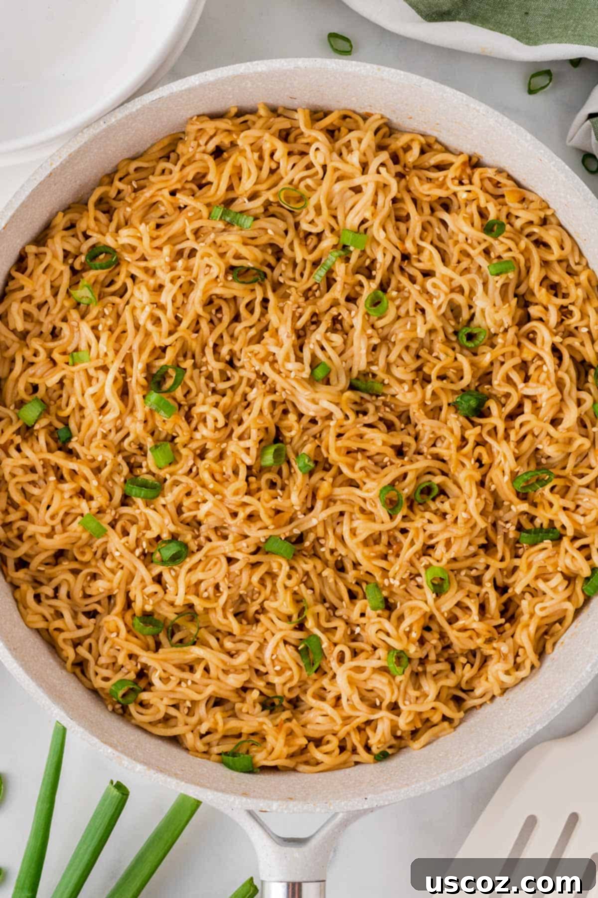 Easy Sesame Garlic Ramen 3 A close-up of garlic ramen noodles shimmering in a skillet, generously topped with vibrant green onions, ready to be served.