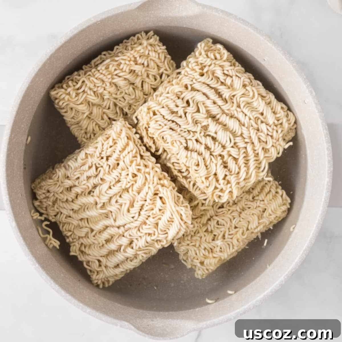 Easy Sesame Garlic Ramen 5 Blocks of instant ramen noodles simmering in a saucepan of boiling water, illustrating the first step of cooking the noodles.