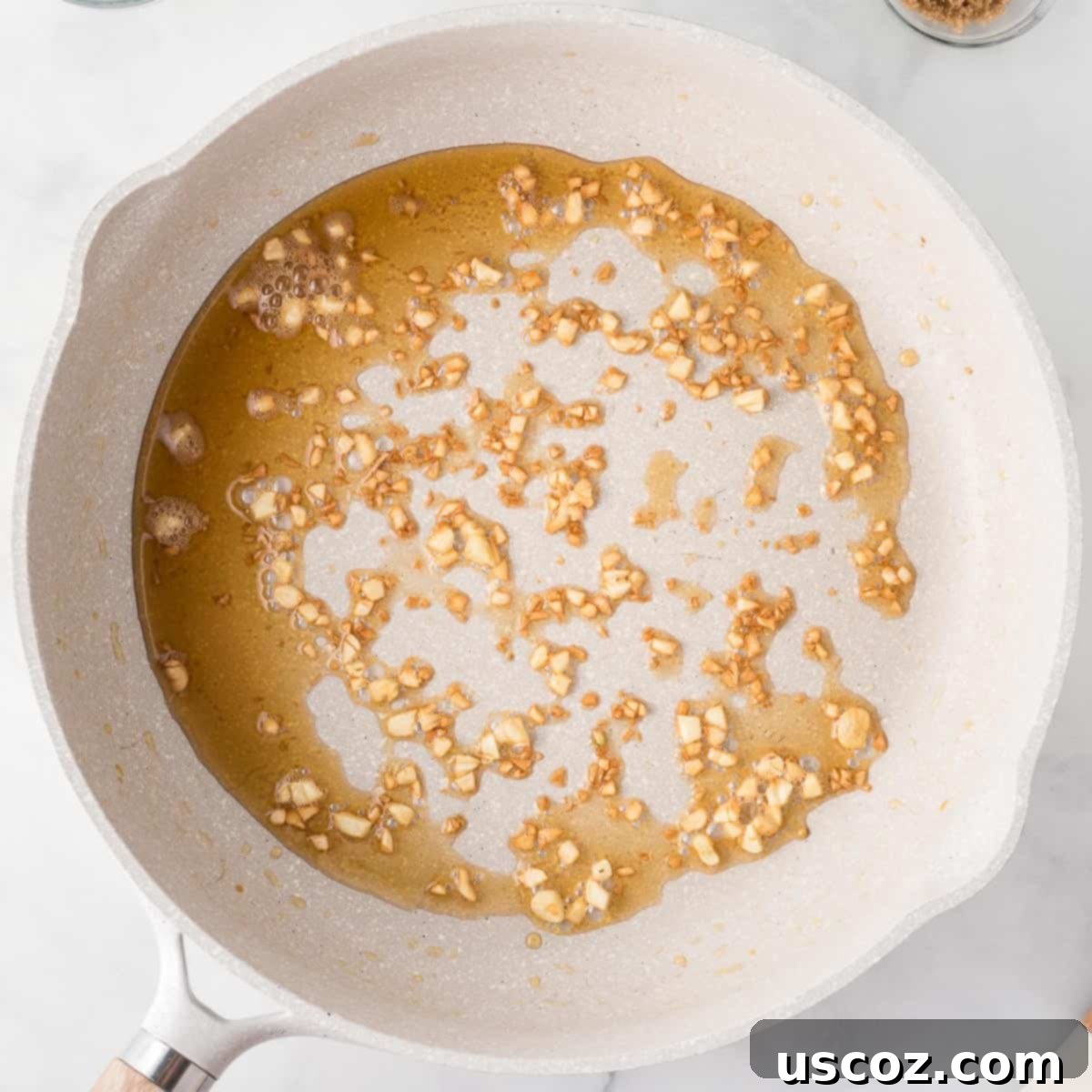 Minced garlic being gently added to a hot skillet containing sesame oil, ready to be sautéed until fragrant.