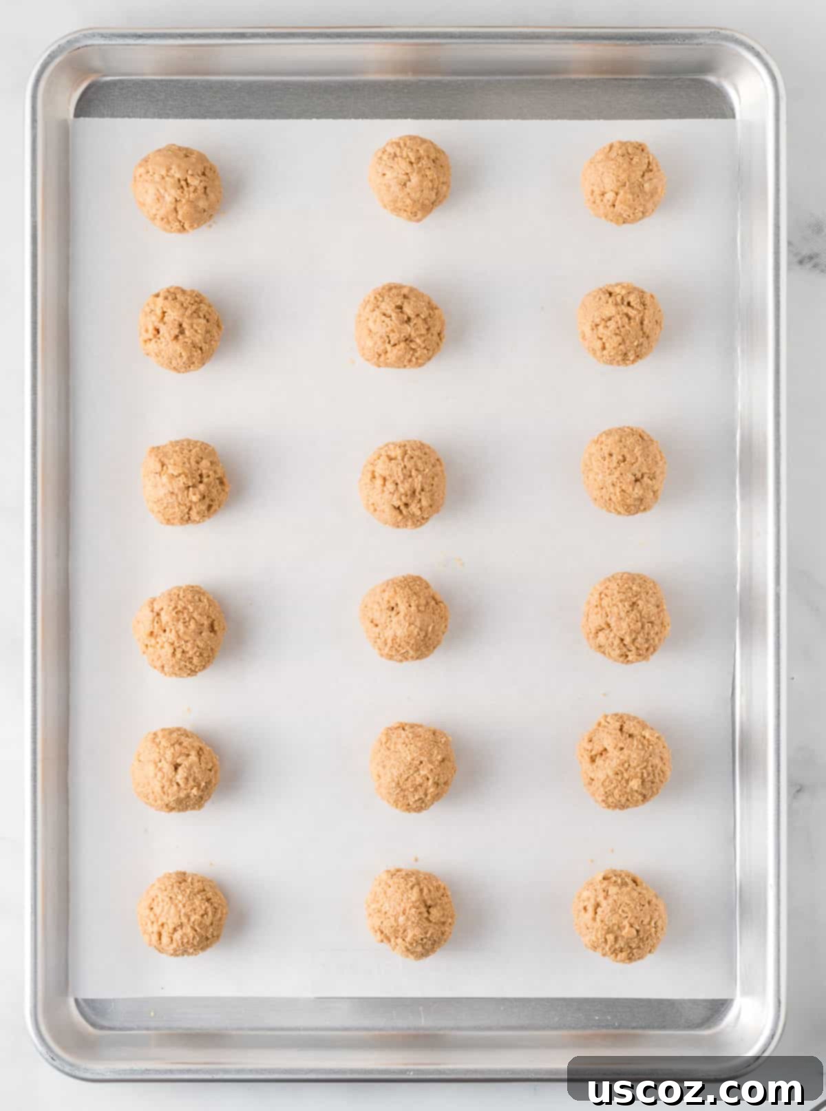 No-Bake Peanut Butter Krispie Treats 7 Rows of un-dipped Rice Krispies peanut butter balls arranged on a parchment-lined baking sheet, chilled and ready for chocolate coating.