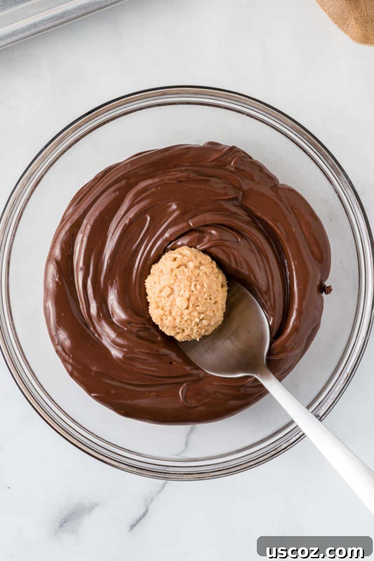 No-Bake Peanut Butter Krispie Treats 8 A close-up shot of a peanut butter ball with Rice Krispies being carefully dipped into a bowl of smooth, melted chocolate.