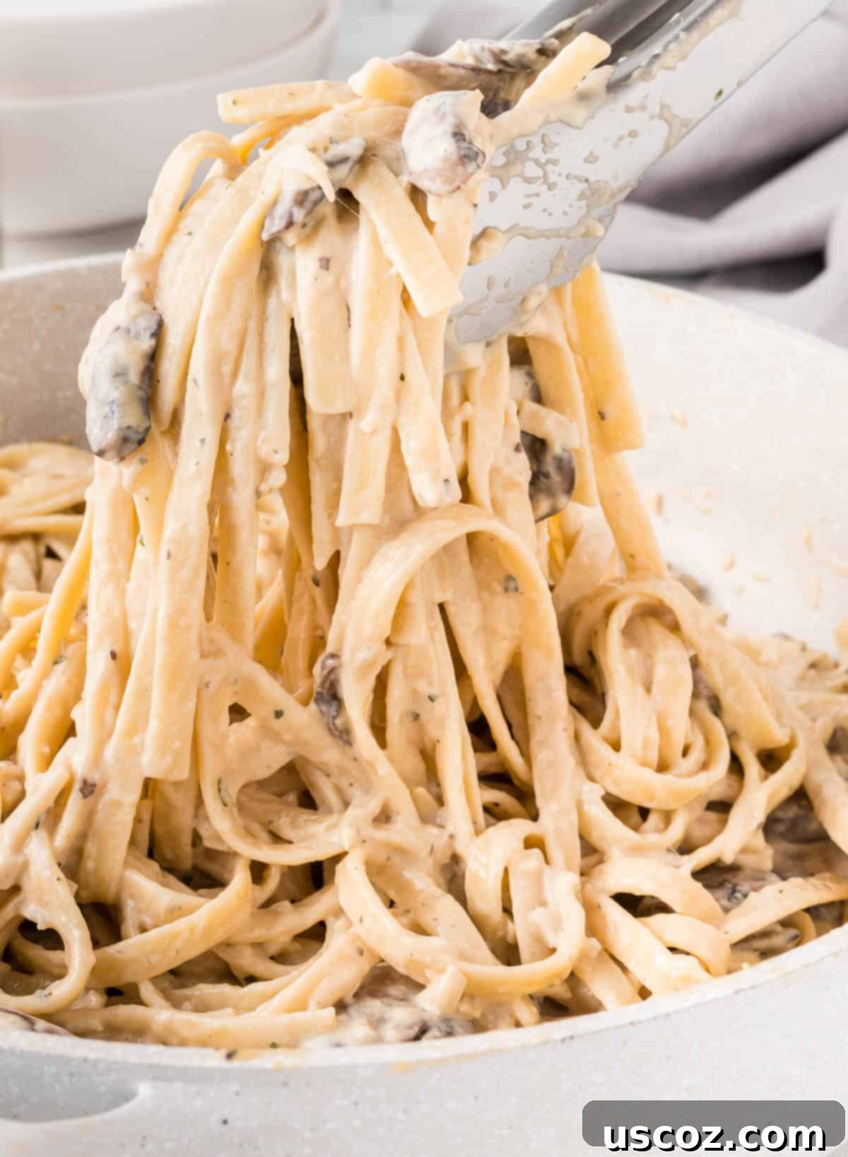 Velvety Mushroom Pasta 3 Tongs lifting a generous serving of creamy mushroom pasta from a skillet, showcasing the rich sauce and tender noodles.