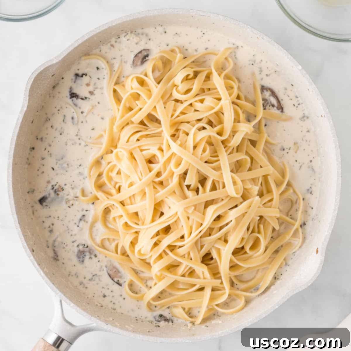 Velvety Mushroom Pasta 9 Cooked fettuccine being added to the creamy mushroom sauce in a skillet, ready to be tossed and combined.