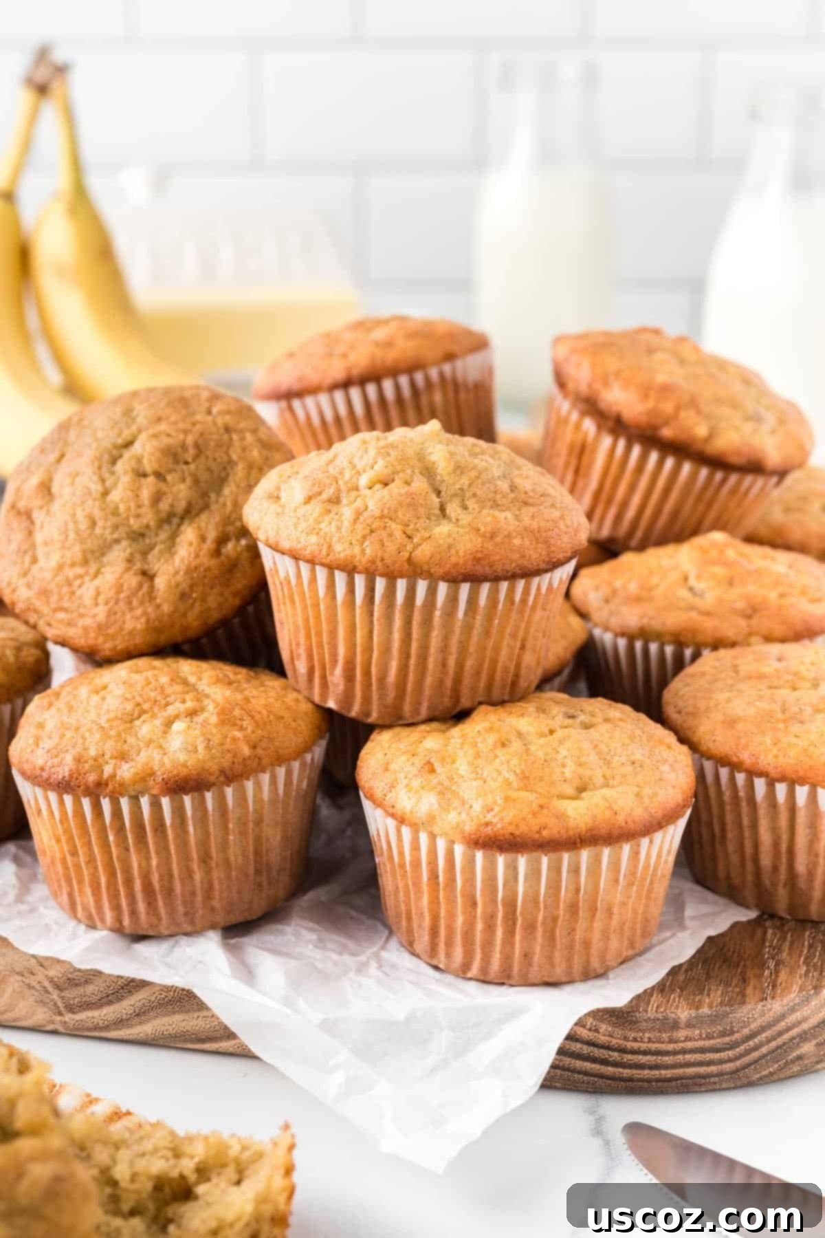 Easy Cake Mix Banana Muffins 2 Stack of fluffy homemade cake mix banana muffins on a wooden board, showcasing their golden tops and soft texture.