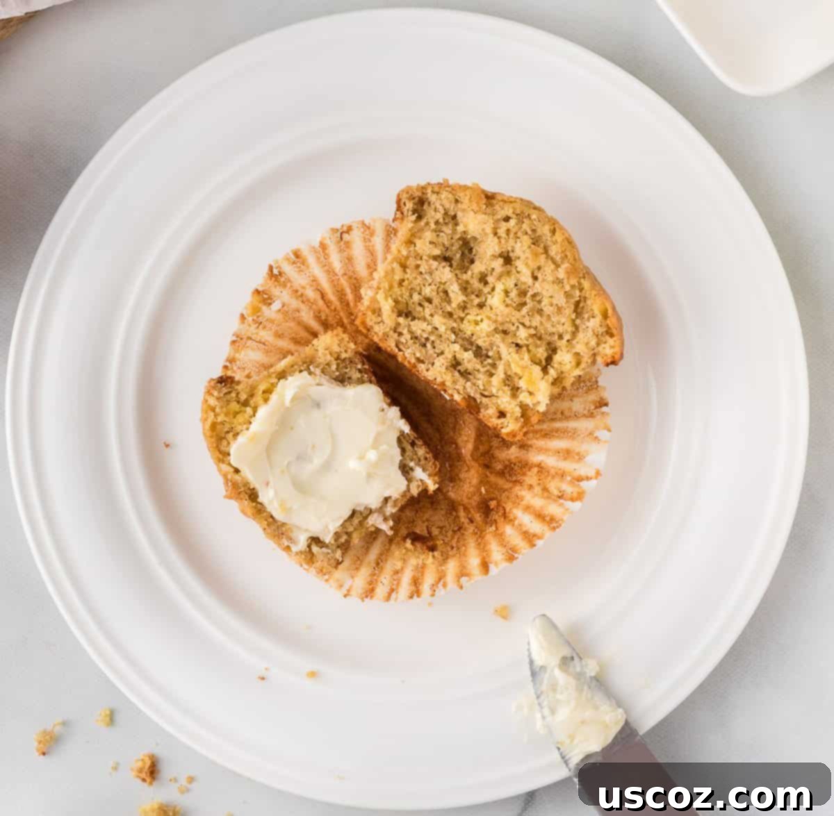 Easy Cake Mix Banana Muffins 14 A fresh banana muffin sliced in half, with a generous spread of butter on one side, ready to be enjoyed as a customizable treat.