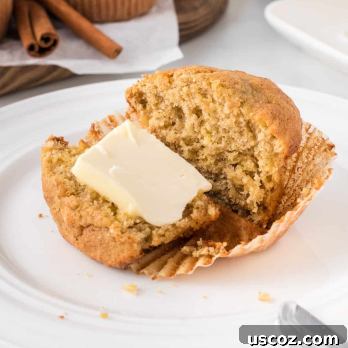 Easy Cake Mix Banana Muffins 3 A perfectly baked banana muffin, cut in half and spread with a dollop of butter, highlighting its moist and tender crumb.