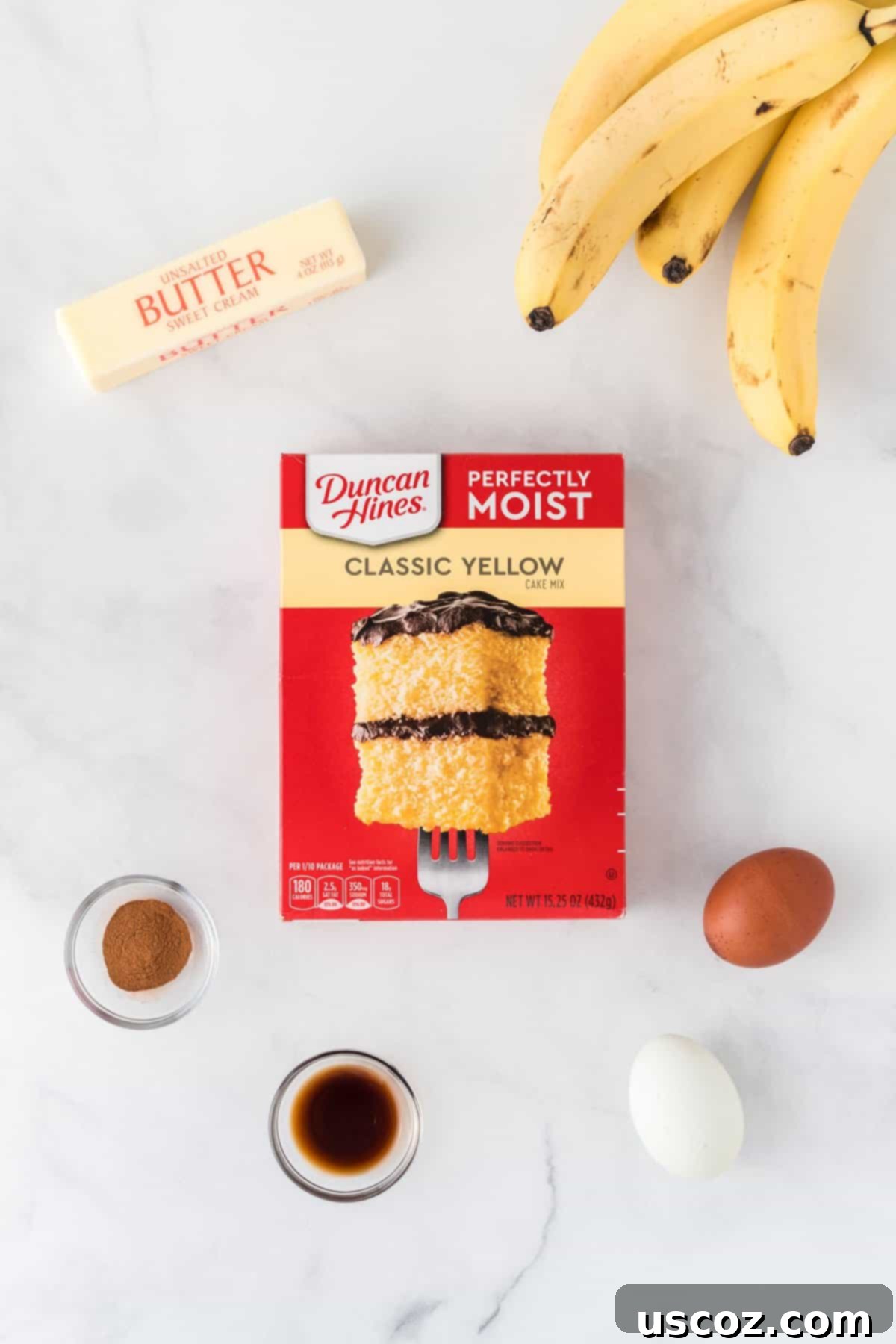 Easy Cake Mix Banana Muffins 4 Collection of ingredients required to make cake mix banana muffins, including a box of yellow cake mix, eggs, vanilla extract, cinnamon, mashed overripe bananas, and melted butter, neatly arranged on a white surface.