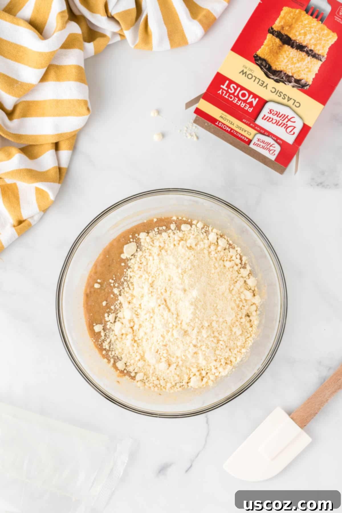 Easy Cake Mix Banana Muffins 7 Pouring a box of yellow cake mix into a bowl containing the wet ingredients for banana muffin batter, ready for gentle mixing.