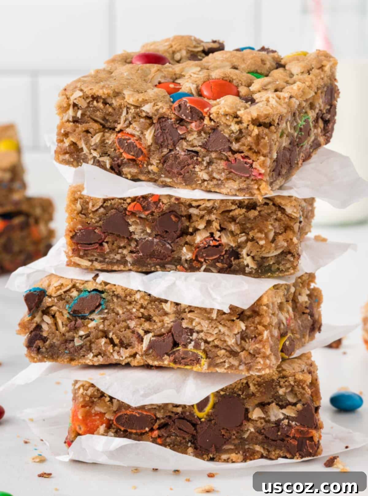 Everything-But-The-Kitchen-Sink Cookie Bars 13 A stack of golden-brown monster cookie bars, neatly separated by pieces of parchment paper, demonstrating perfect storage or presentation.
