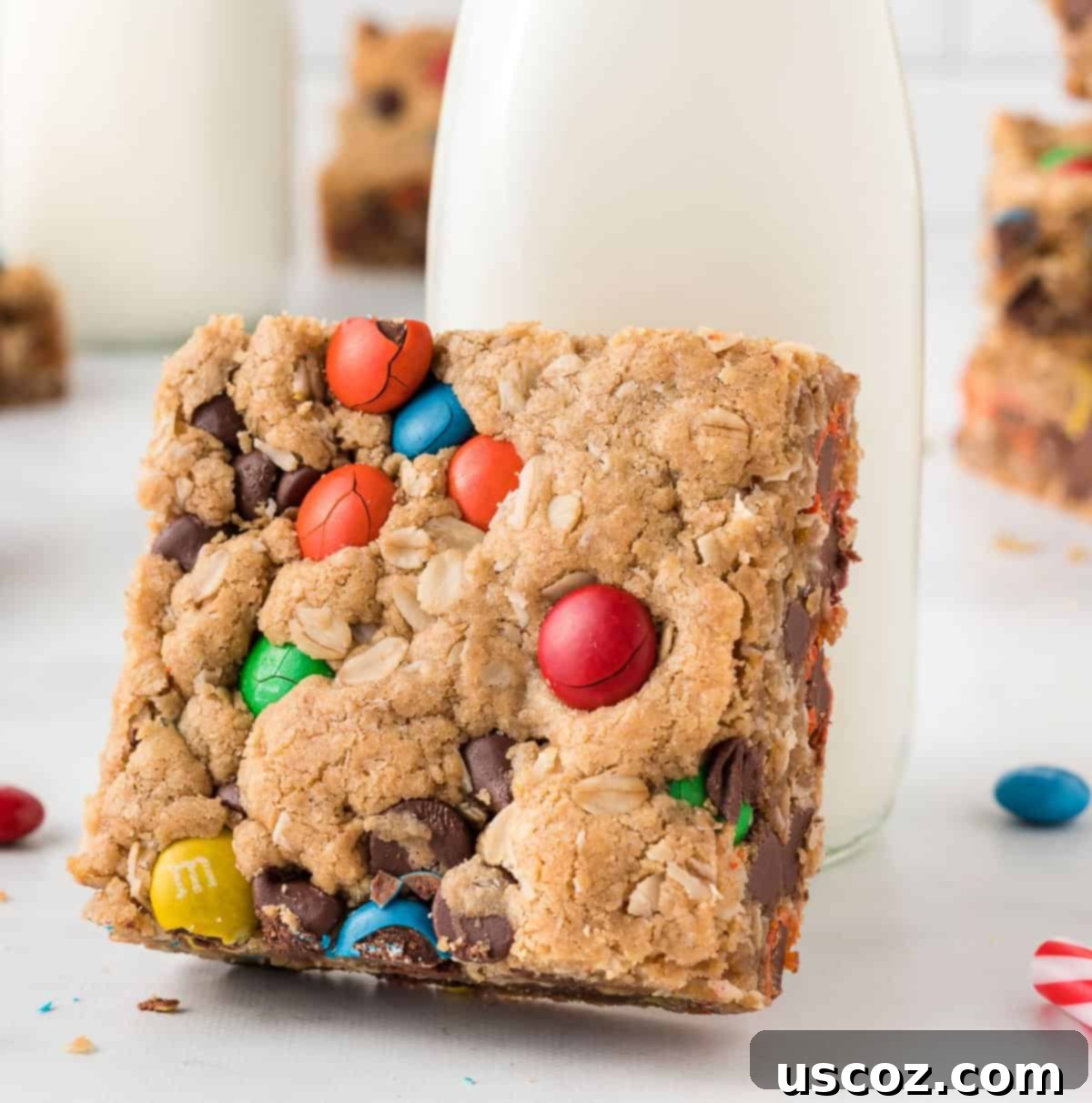 Everything-But-The-Kitchen-Sink Cookie Bars 14 A single monster cookie bar propped up invitingly on a glass of milk, emphasizing its perfect pairing for a sweet treat.