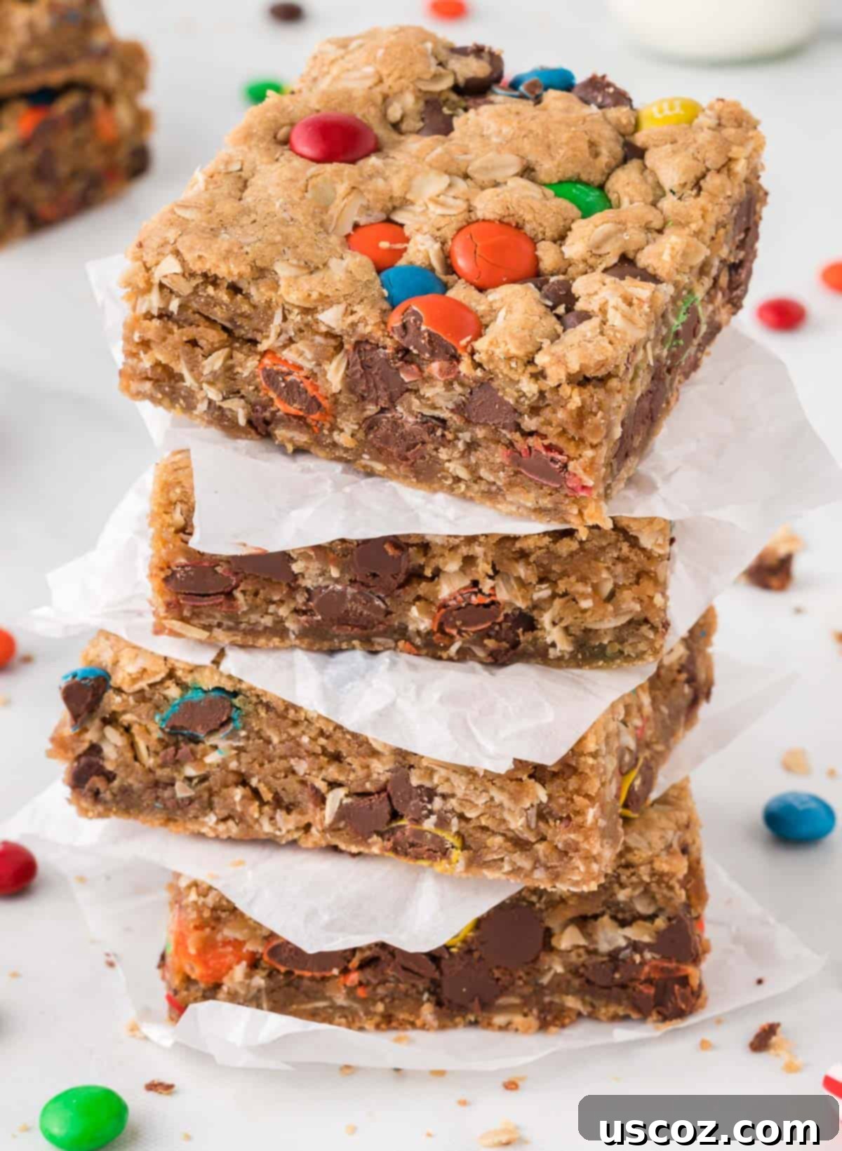 Everything-But-The-Kitchen-Sink Cookie Bars 3 Stack of freshly baked Monster Cookie Bars separated by parchment paper, showcasing their thick, chewy texture and colorful M&M's.