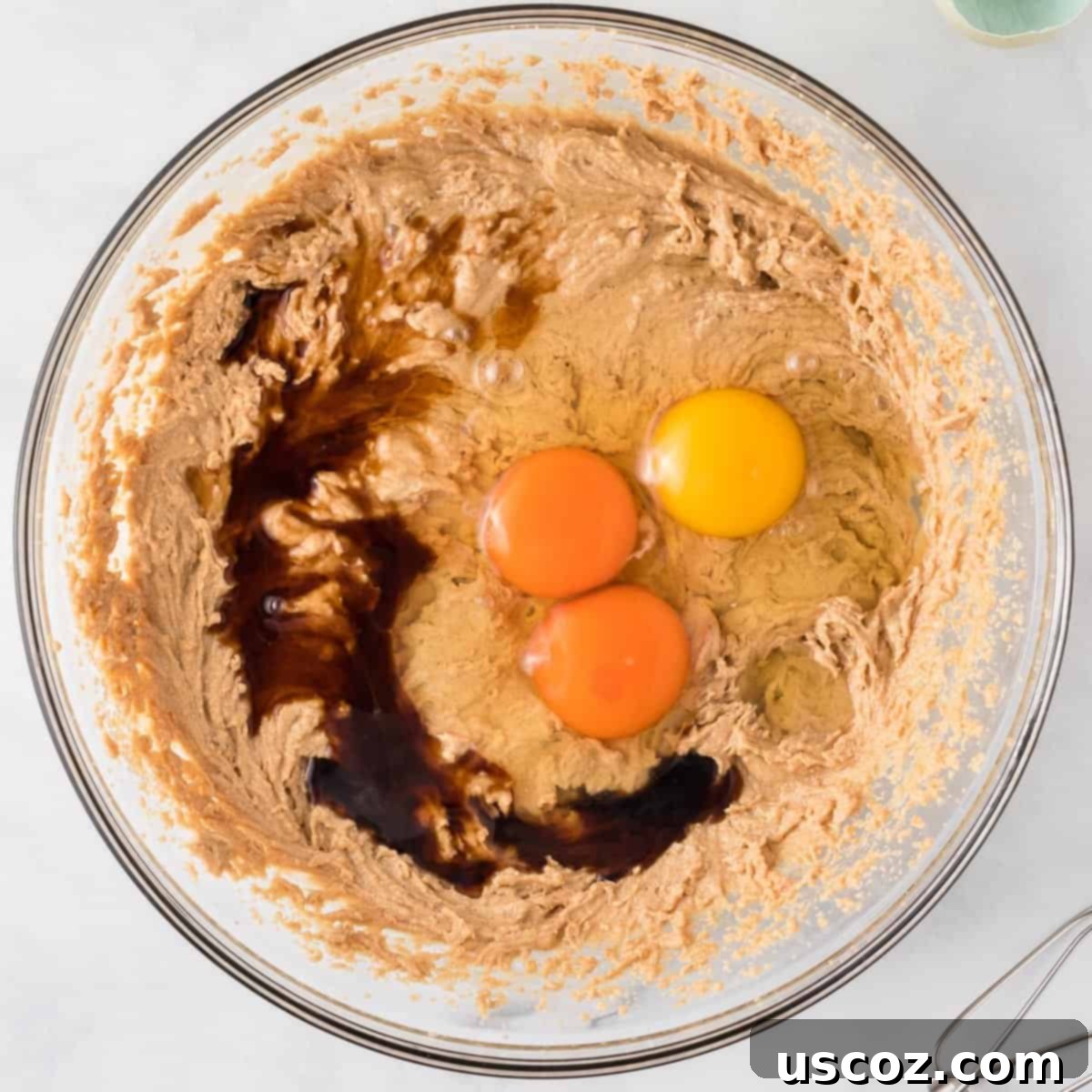 Everything-But-The-Kitchen-Sink Cookie Bars 7 The wet ingredients for monster cookie bars, showing eggs and vanilla extract being added to the creamy batter, ensuring a well-blended mixture.