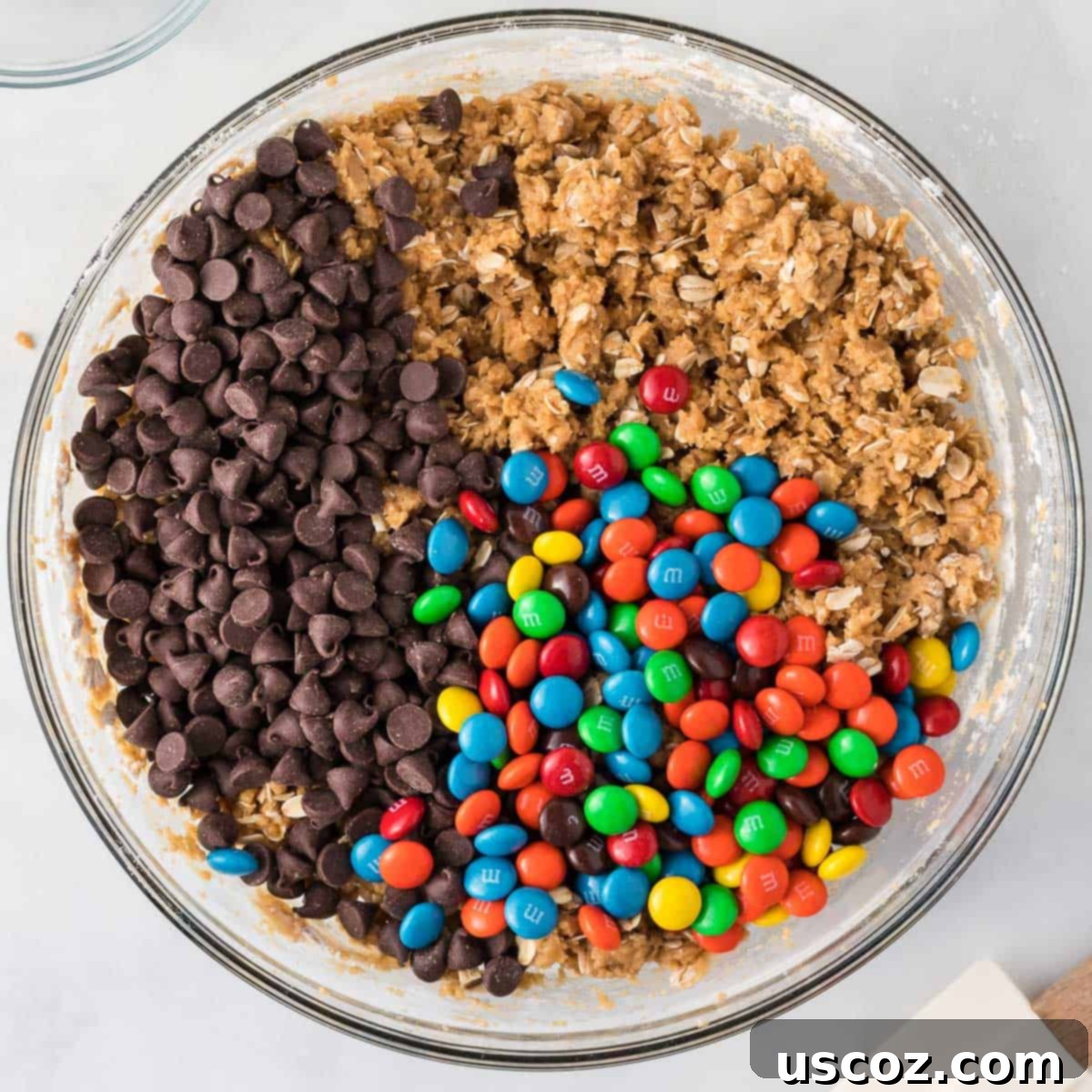 Everything-But-The-Kitchen-Sink Cookie Bars 9 Chocolate chips and M&M's being gently folded into the monster cookie bar batter, ensuring an even distribution of the delicious mix-ins.