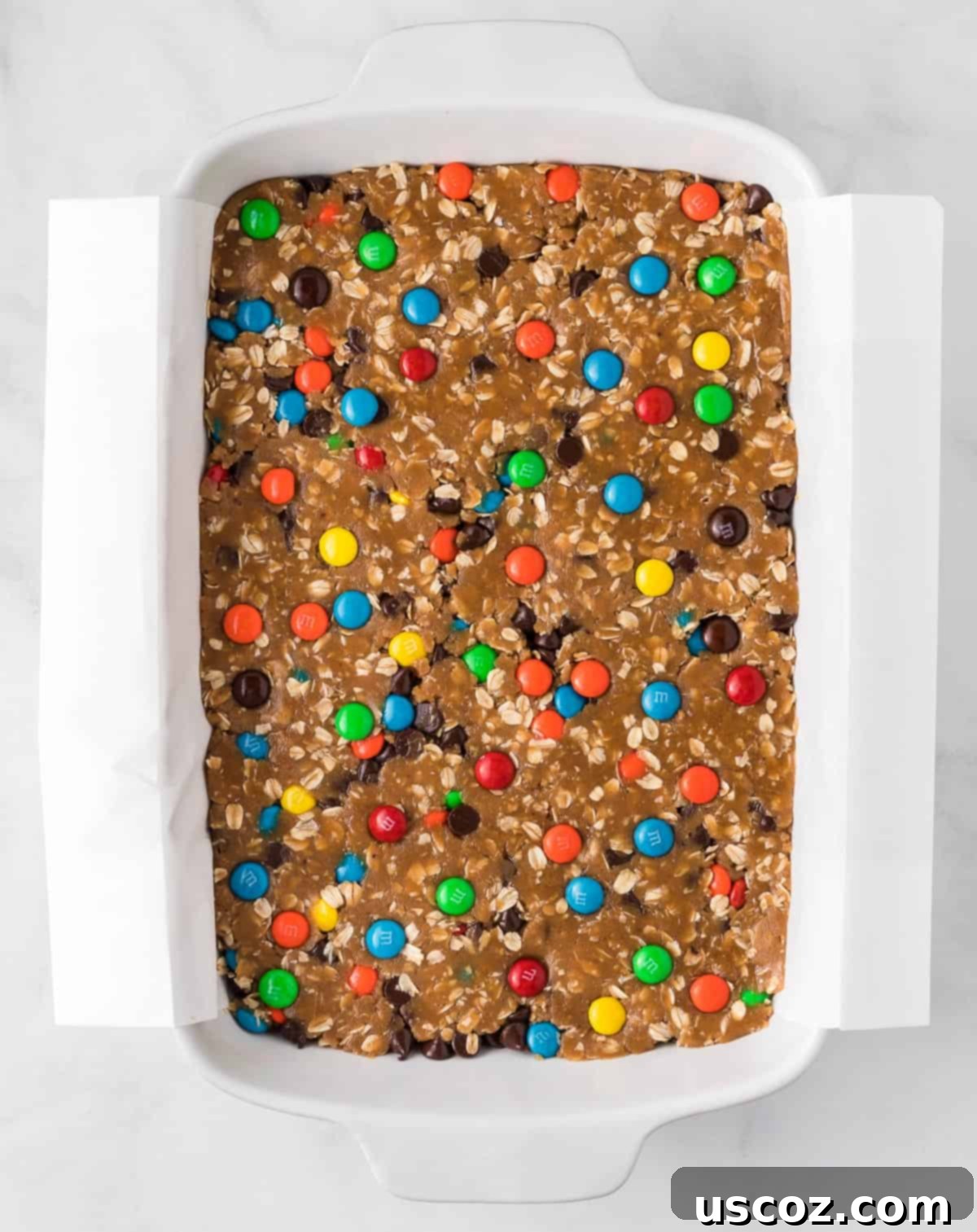 Everything-But-The-Kitchen-Sink Cookie Bars 10 The monster cookie bar batter, studded with colorful M&M's and chocolate chips, perfectly pressed into a parchment-lined baking dish, ready for the oven.