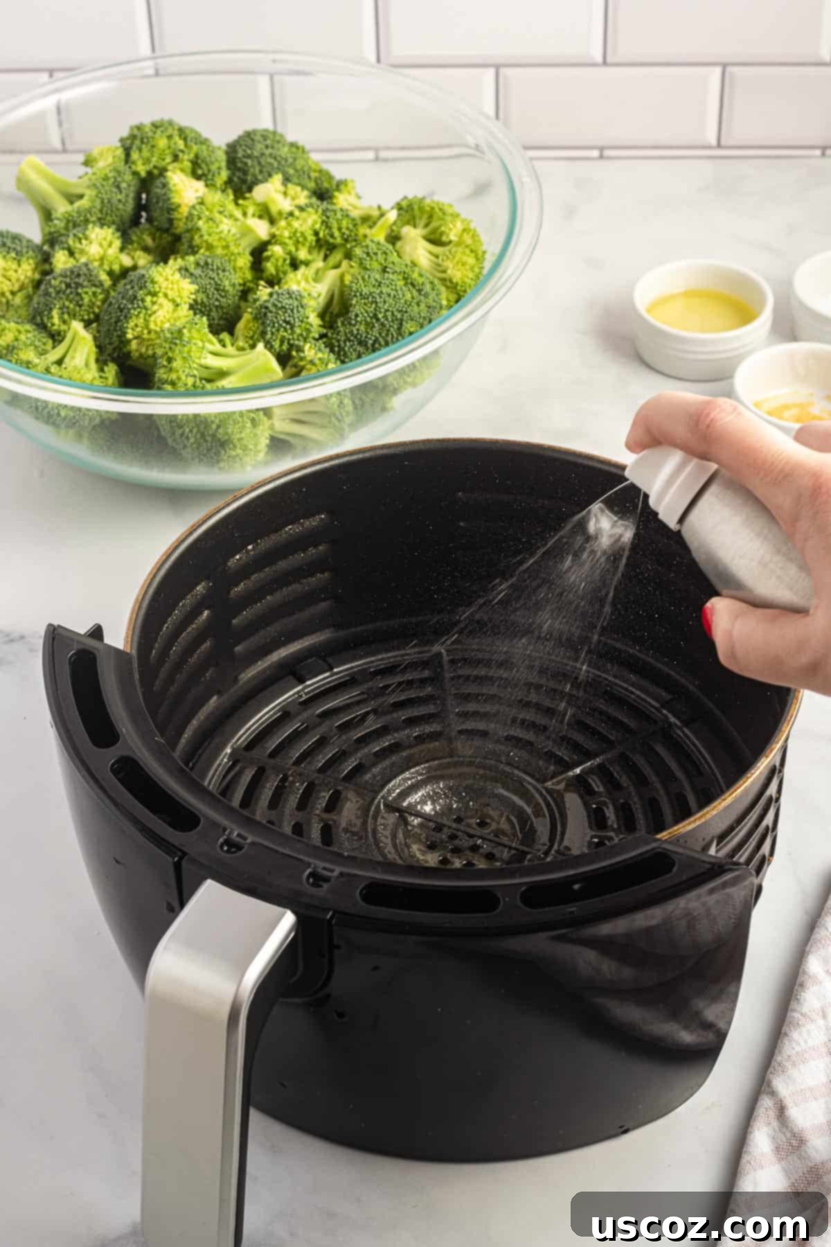 Perfectly Crispy Air Fryer Broccoli 4 Close-up shot of an air fryer basket being sprayed with olive oil, preparing it for the broccoli.