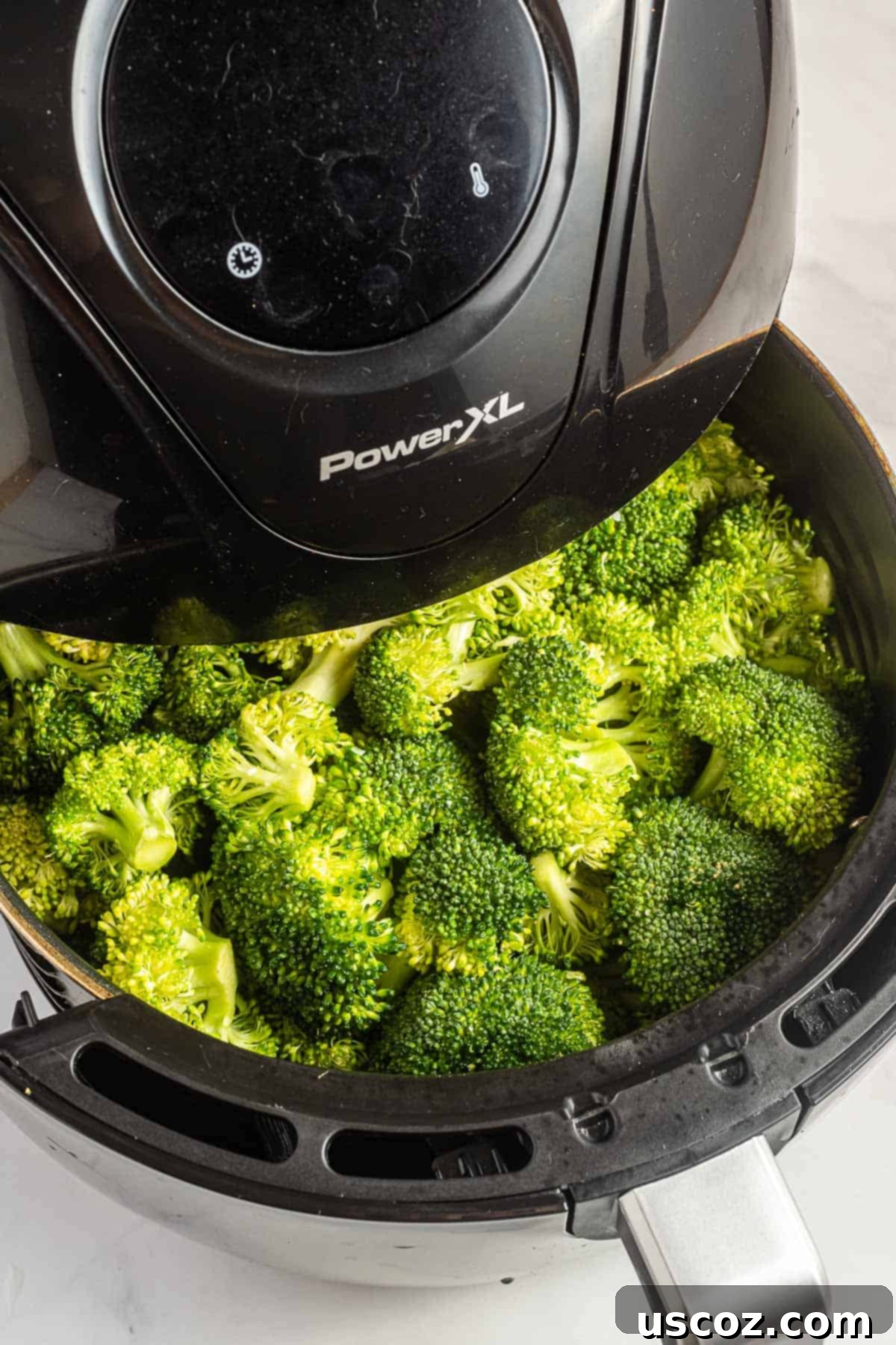 Perfectly Crispy Air Fryer Broccoli 5 Broccoli florets cooking and crisping up inside an air fryer basket, with visible browned edges.
