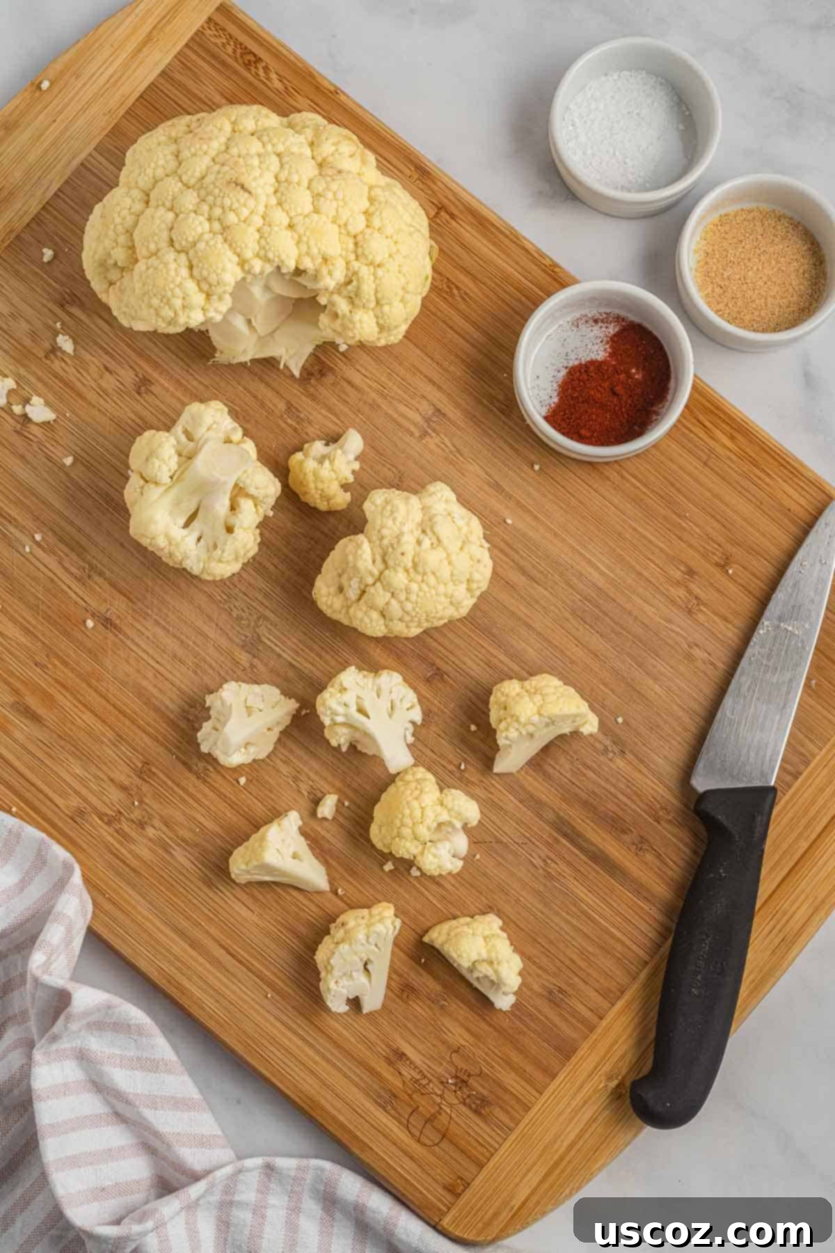 Crispy Air Fryer Cauliflower 4 A person cutting a head of cauliflower into small, uniform florets on a cutting board.
