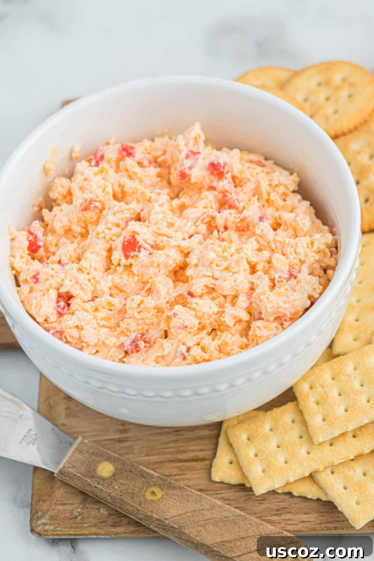 Pimento Cheese 2 Creamy homemade pimento cheese dip served with a variety of crackers on a rustic wooden board, ready for a gathering.