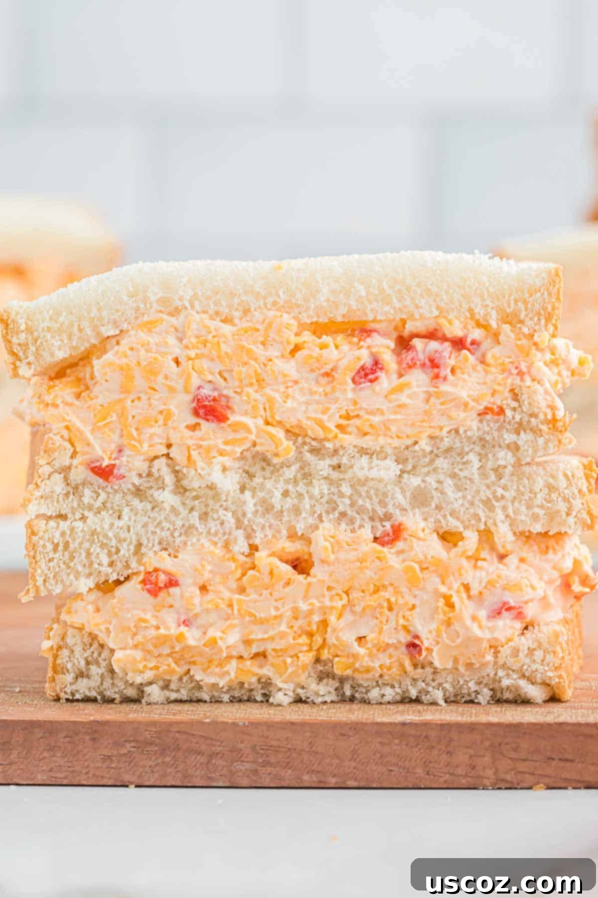 Pimento Cheese 11 Two pimento cheese sandwiches, freshly made and cut in half, stacked neatly on a plate, showcasing the thick, vibrant filling and soft texture.