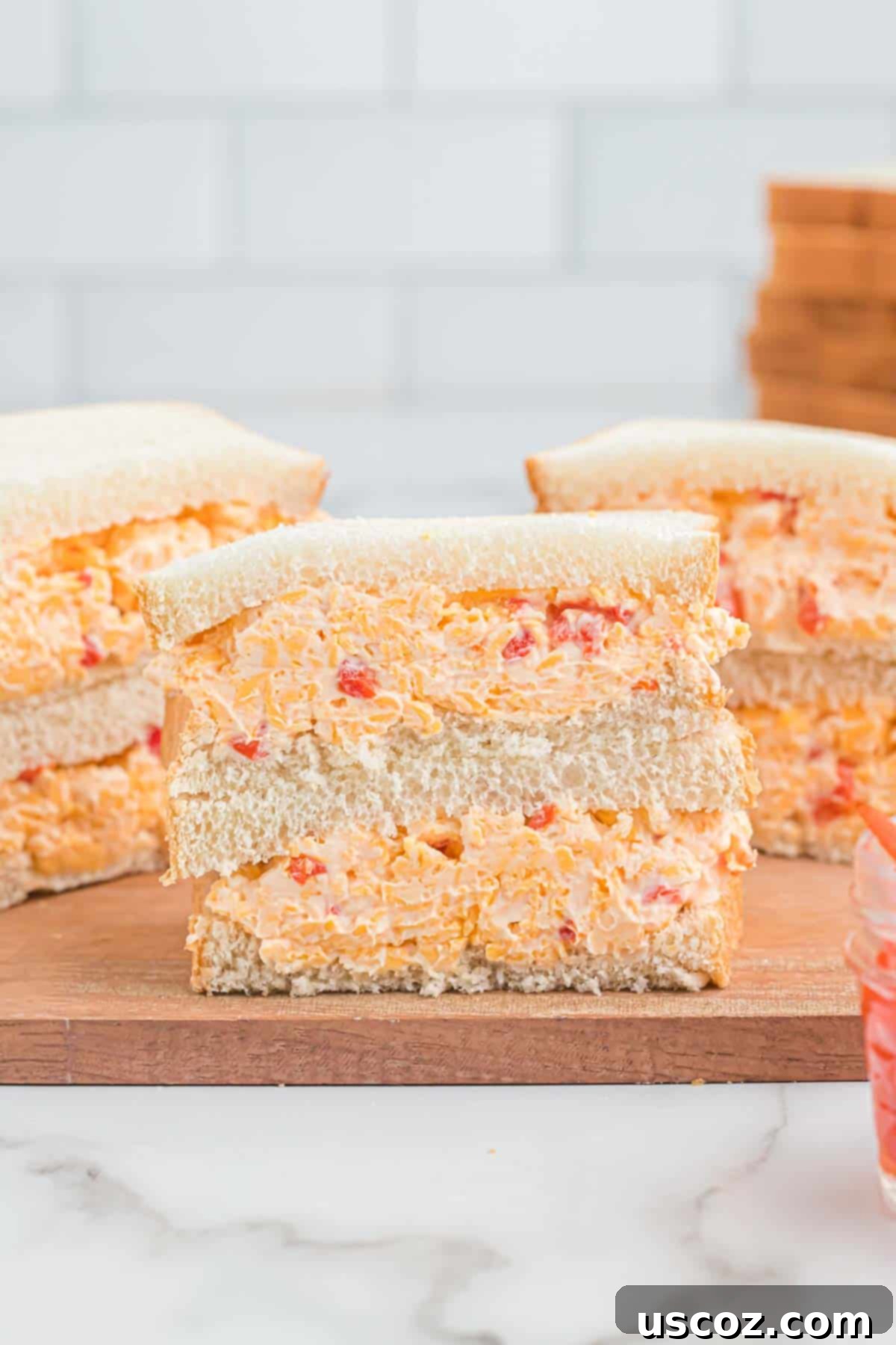 Pimento Cheese 3 A freshly made pimento cheese sandwich, cut diagonally in half and stacked, showcasing the generous, creamy filling and soft white bread.